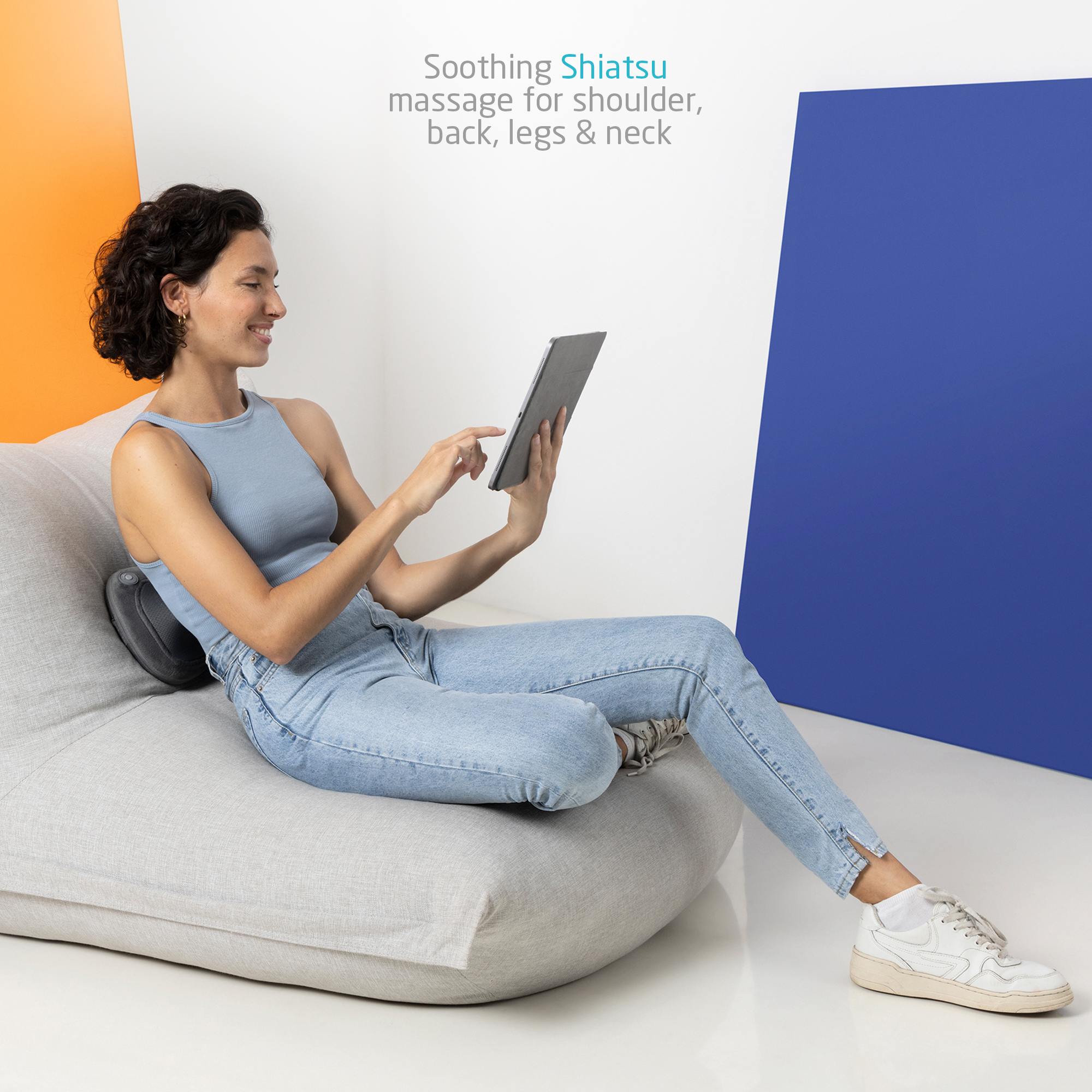 Kobieta używająca tabletu siedząc na worku sako z poduszką do masażu za nią.