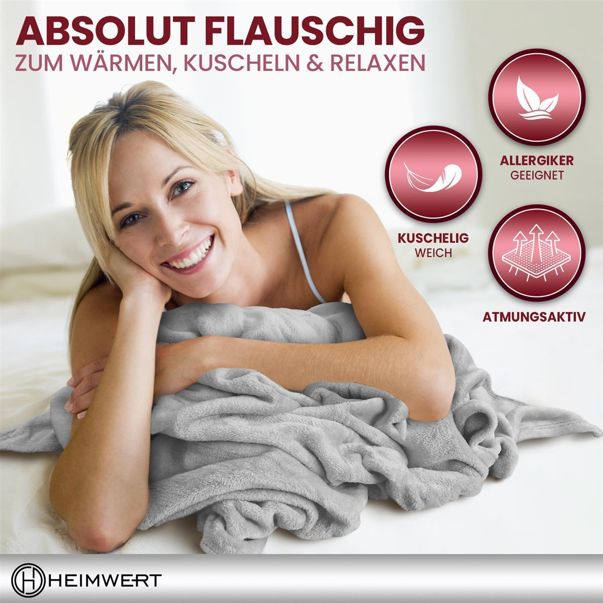 Eine Frau entspannt sich, lächelt und ist in eine graue Decke gehüllt.