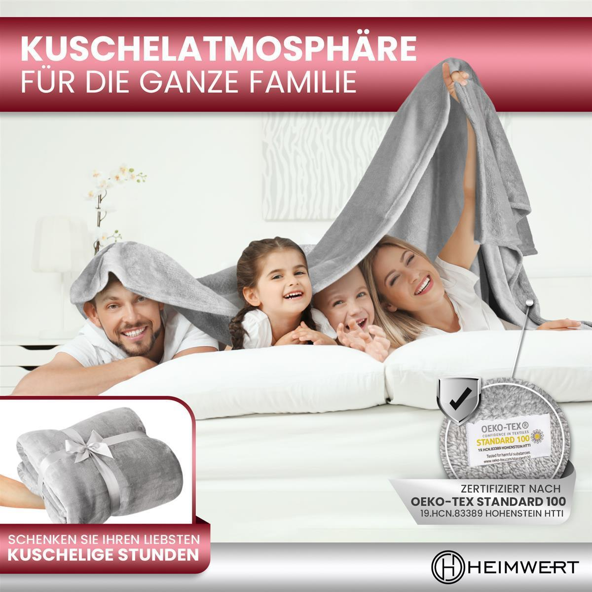 Eine vierköpfige Familie spielt unter einer grauen Decke auf einem Bett.