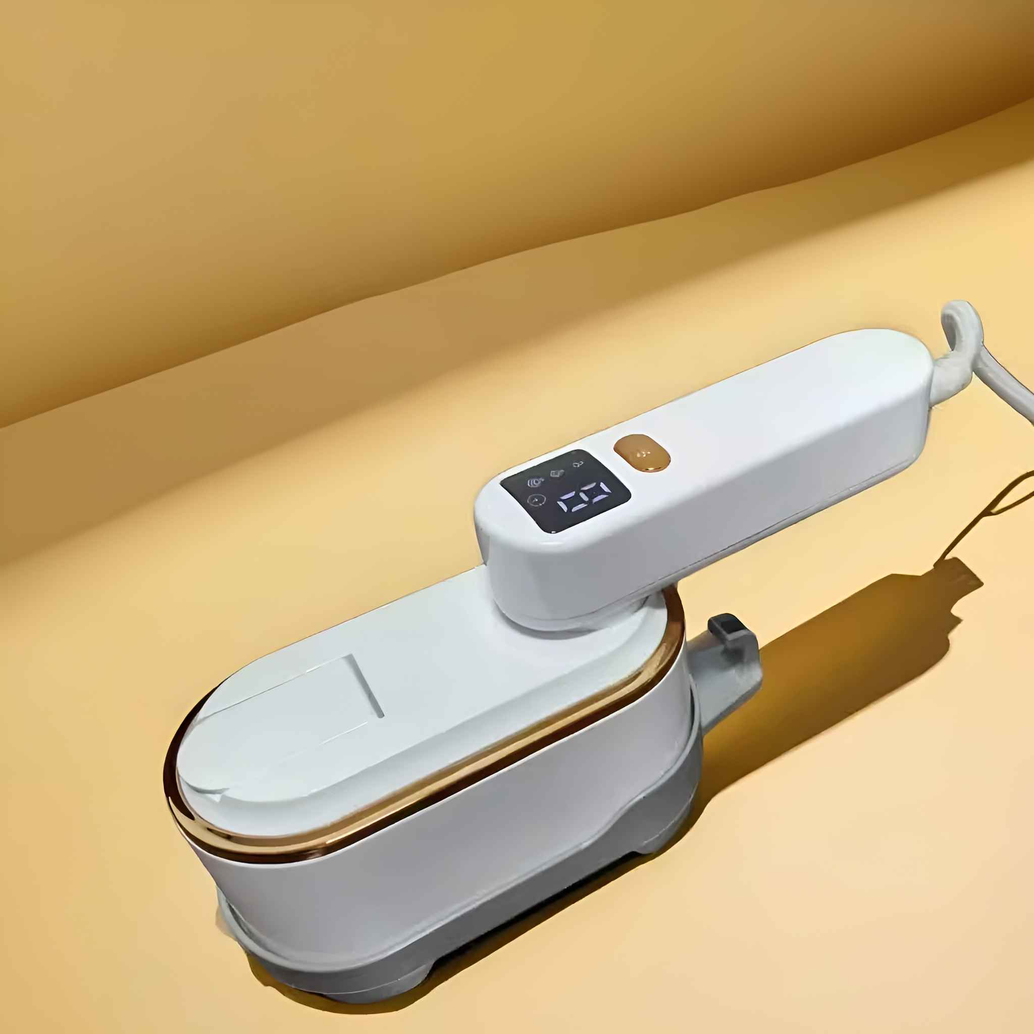 Ein weißes und goldenes Mini-Bügeleisen mit digitaler Anzeige. Es liegt auf einer gelben Oberfläche.