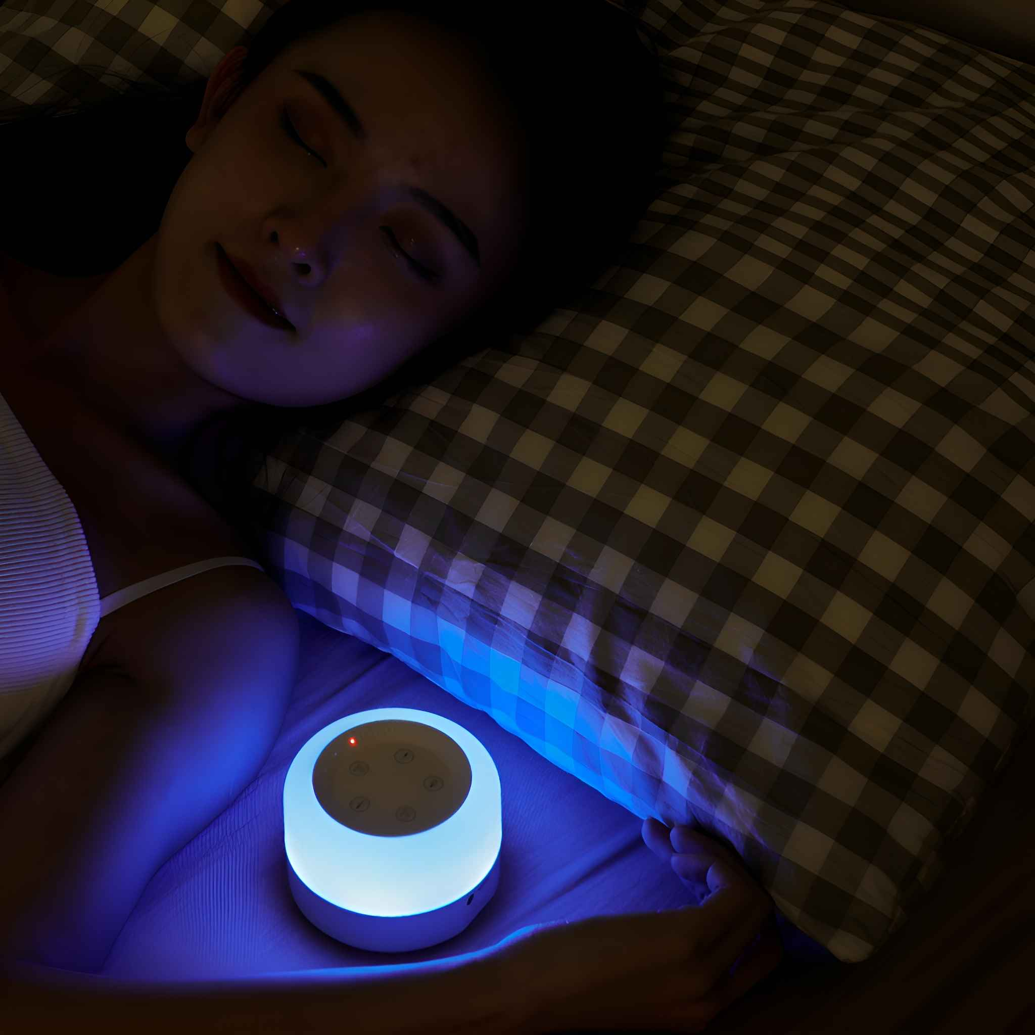 Eine schlafende Frau mit einer Nachttischlampe. Die Lampe emittiert blaues Licht. Ein kariertes Kissen ist sichtbar.