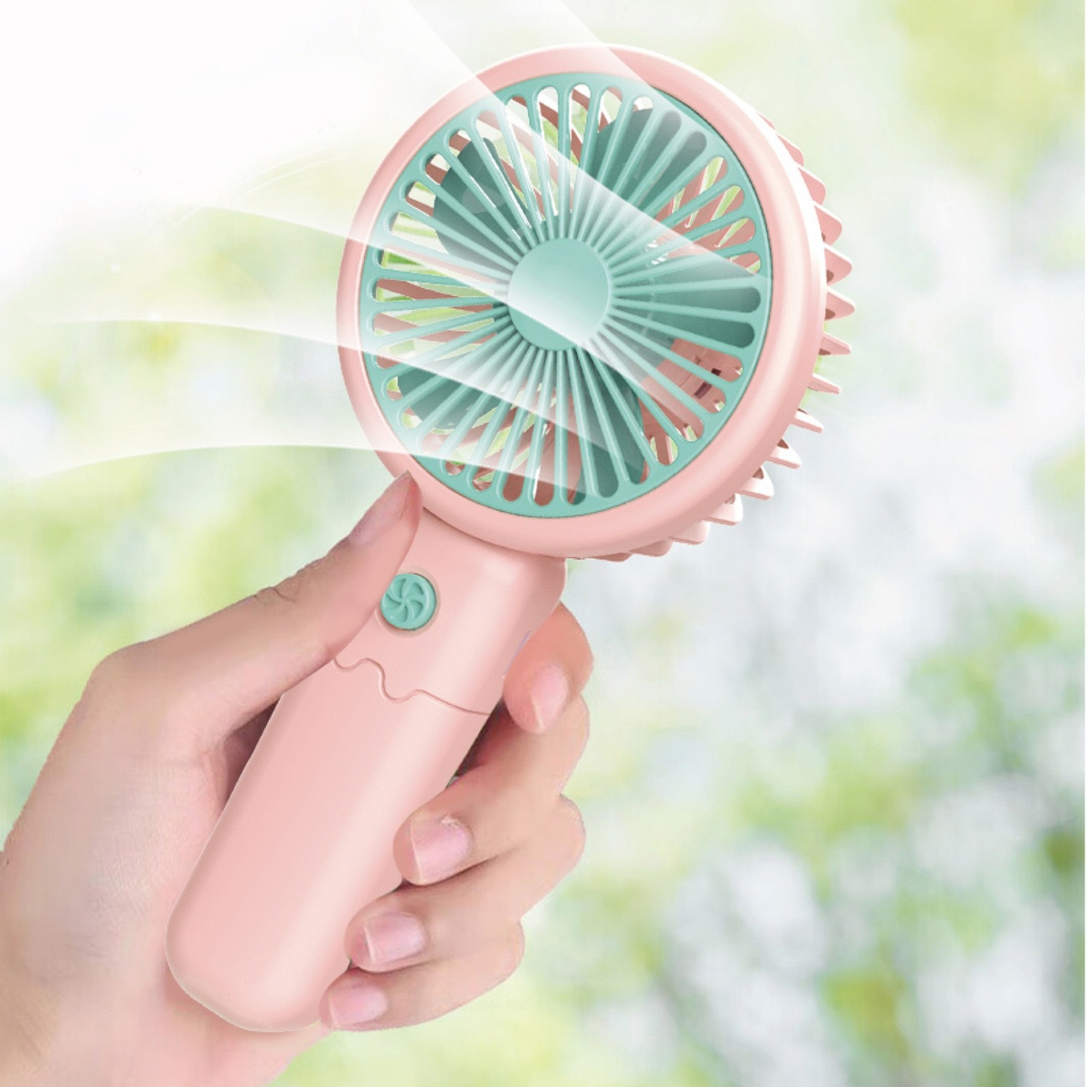 Eine Hand, die einen rosa Handventilator hält. Der Ventilator hat einen grünen Ventilator und bläst Luft.