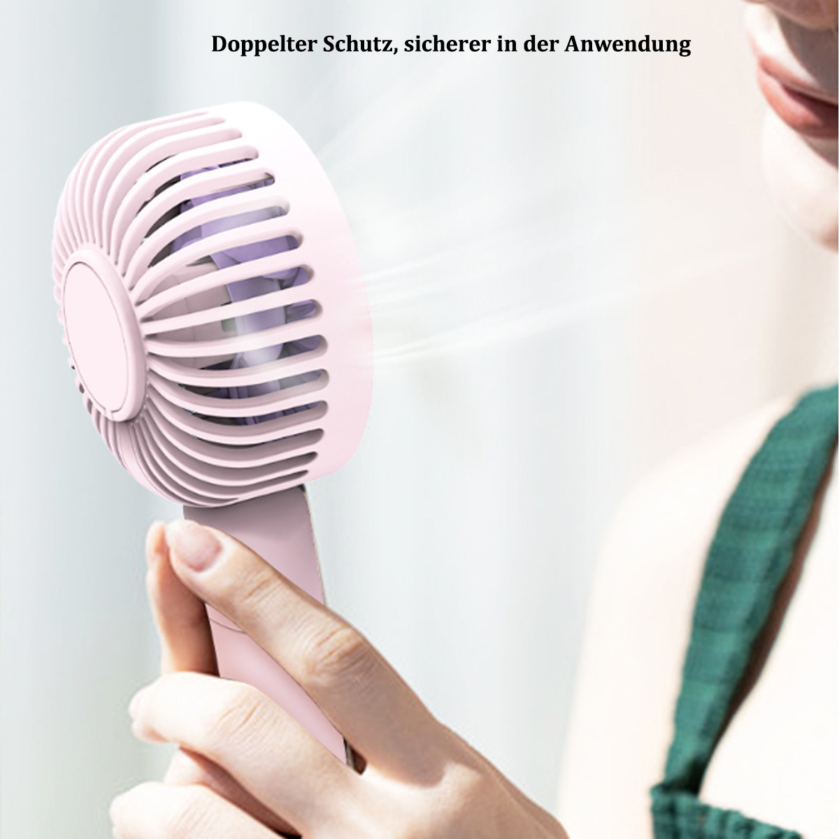 Eine Frau hält einen pinkfarbenen tragbaren Ventilator. Der Ventilator ist an und es wird Luft geblasen. Sie trägt ein grünes Oberteil.