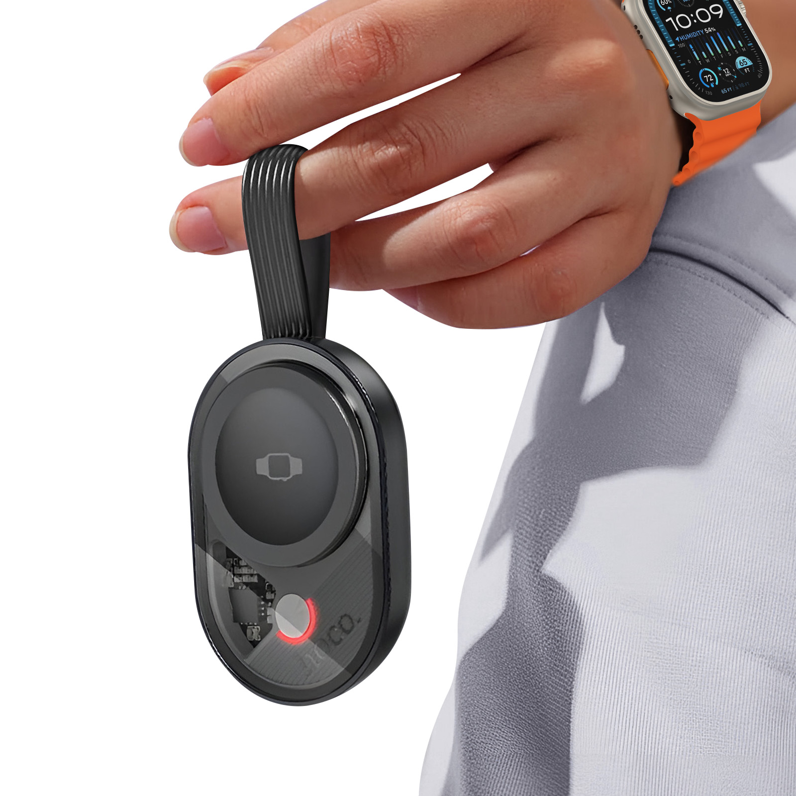 Eine Person hält ein schwarzes Ladegerät mit Riemen in der Nähe einer Apple Watch. Die Uhr hat ein orangefarbenes Band.