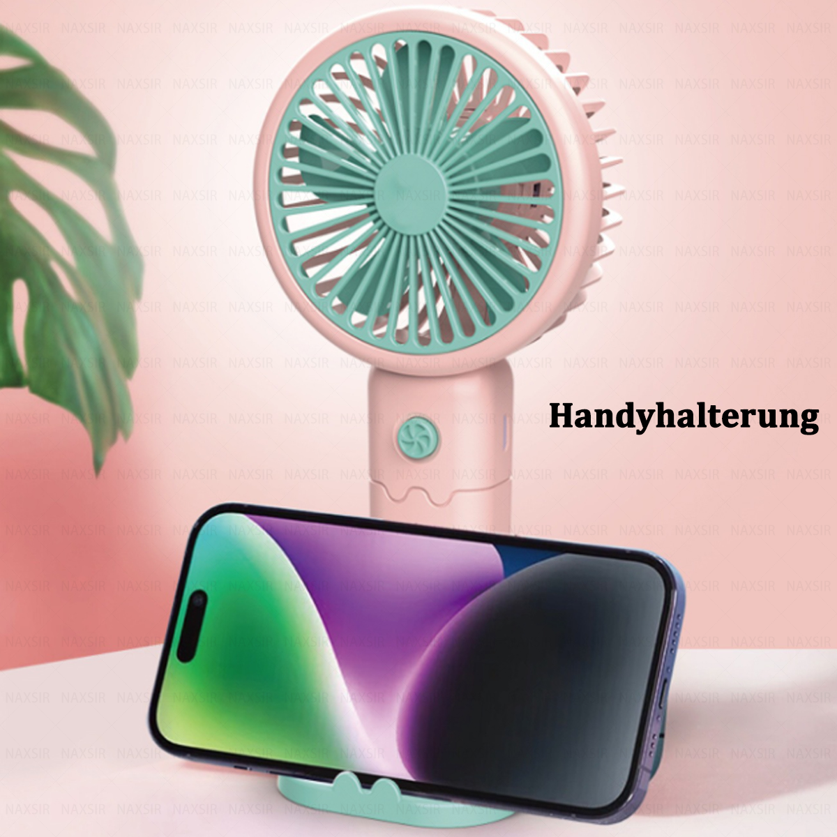 Rosa-Türkis-Ventilator mit Telefon auf weißer Oberfläche, Blatt im Hintergrund.