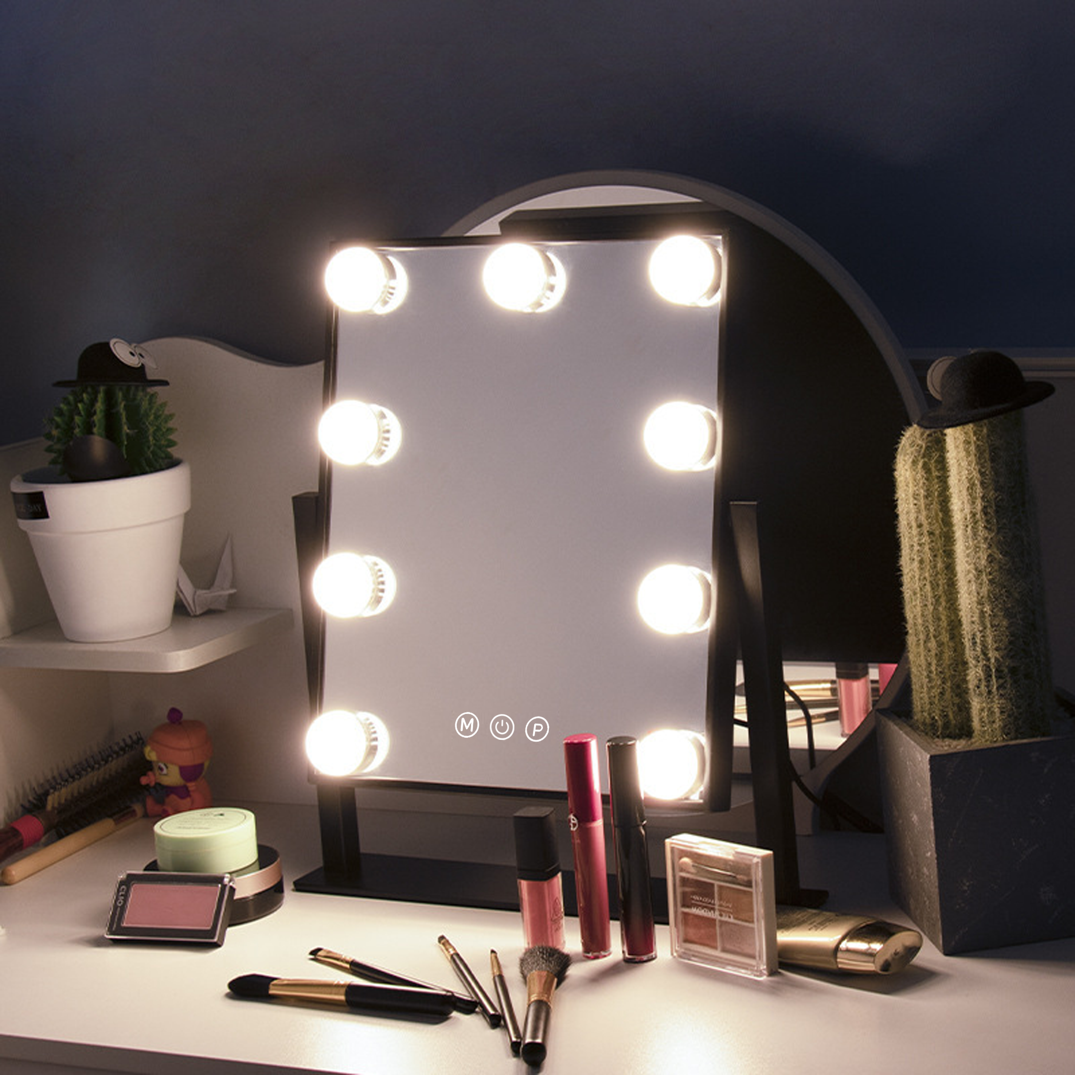 Ein beleuchteter rechteckiger Schminkspiegel auf einem weißen Tisch. Make-up-Produkte sind sichtbar, rechts ein Kaktus.