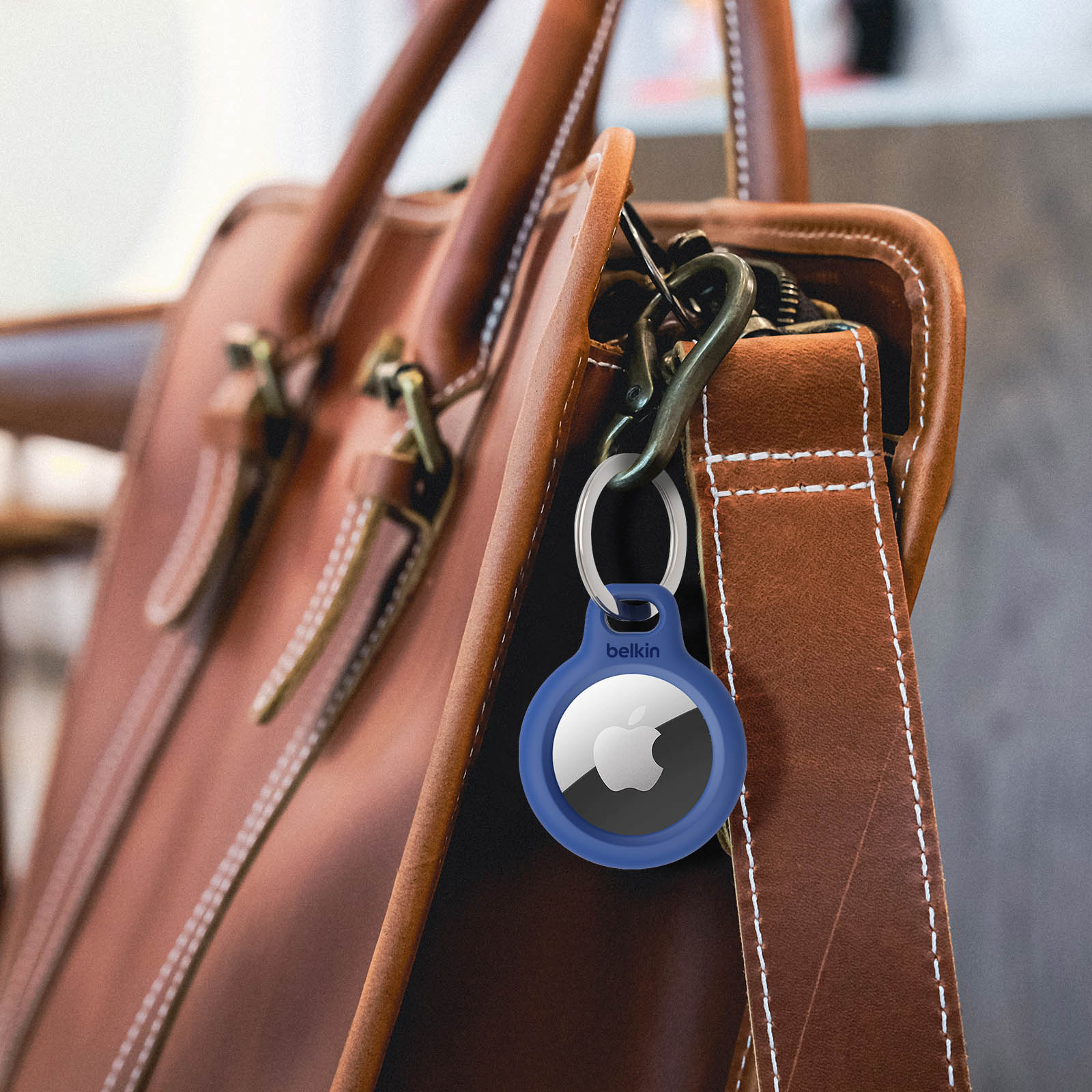 Niebieski Belkin AirTag z brelokiem przymocowanym do brązowej skórzanej torby, pokazujący srebrne logo Apple.