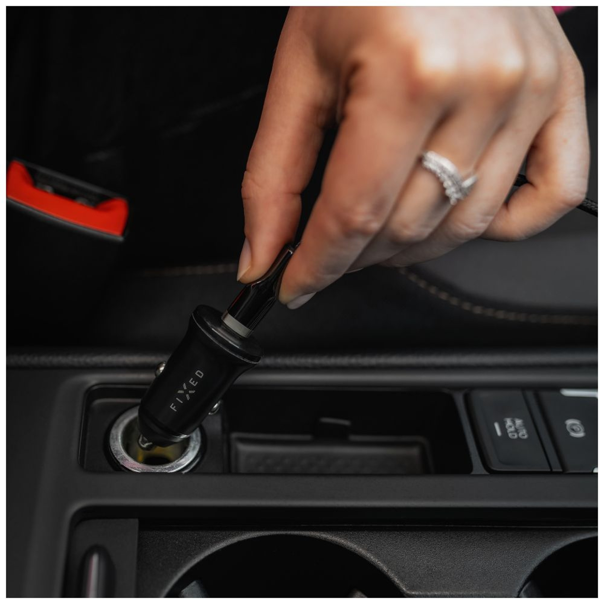 Eine Hand steckt ein schwarzes Autoladegerät in den Zigarettenanzünder eines Autos. Auf dem Ladegerät steht 'FIXED'.