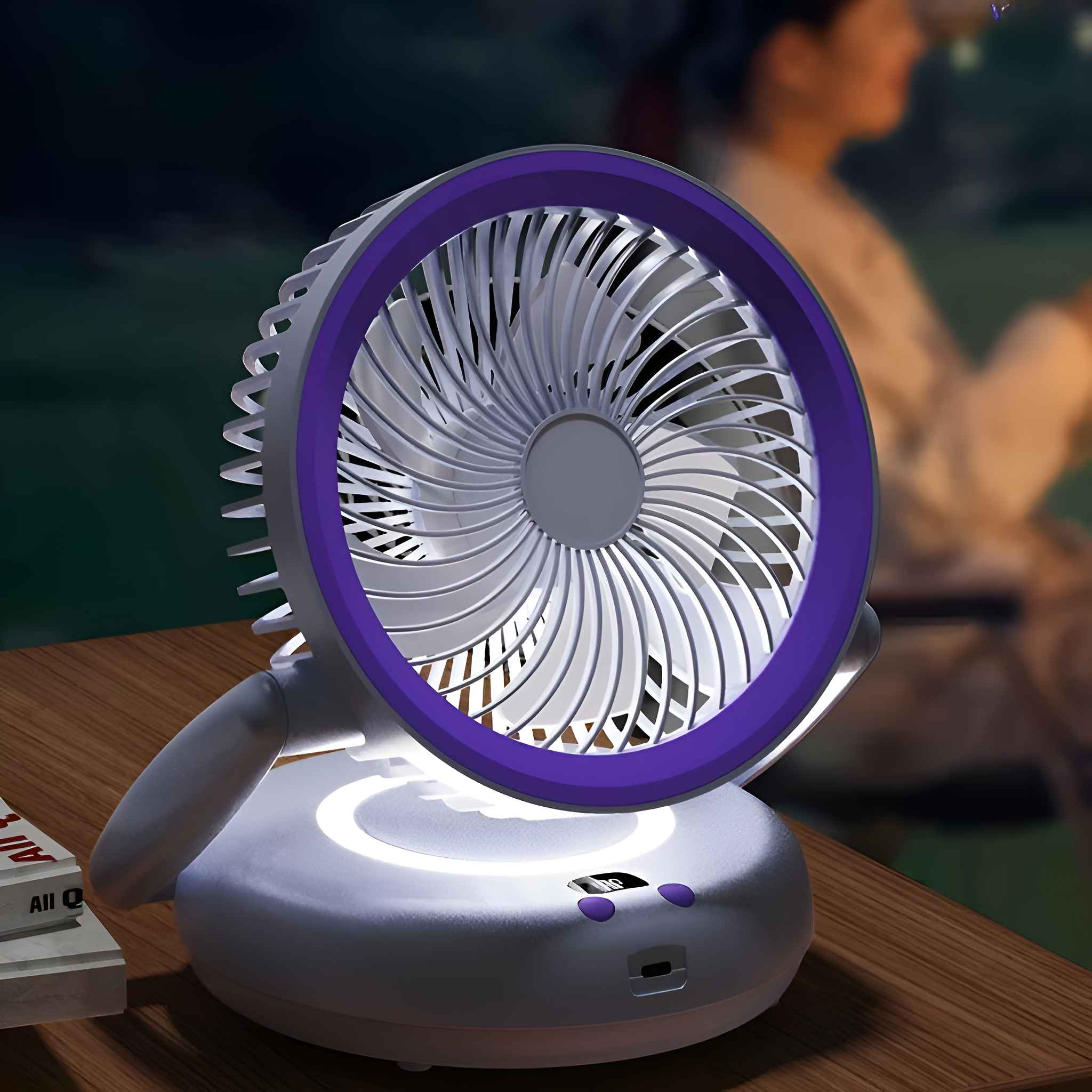 Ein weißer und lila Ventilator auf einer Holzoberfläche. Der Ventilator hat einen lila Lichtring. Es gibt ein Buch.