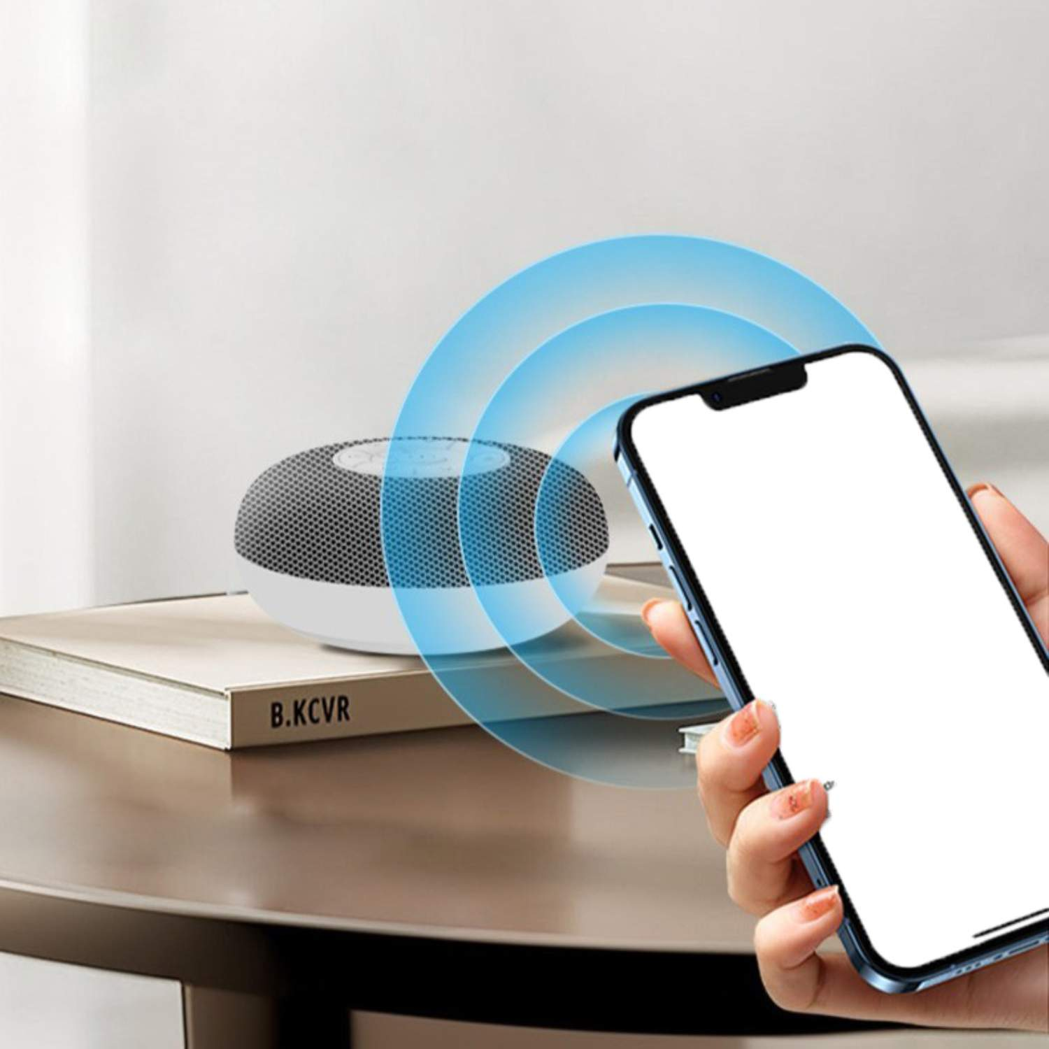 Ein kleiner, runder Lautsprecher auf einem Buch, neben einem Smartphone. Blaue Bögen gehen vom Lautsprecher aus.