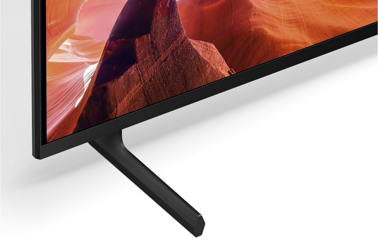 Zbliżenie podstawki telewizora przedstawiającej czarną, sześciokątną podstawę podtrzymującą ekran z krajobrazem kanionu.