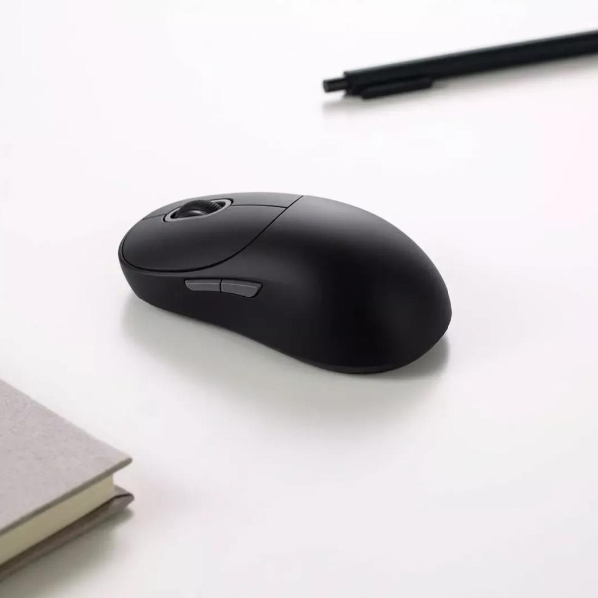 Mouse nero su superficie bianca con penna e libro sullo sfondo.