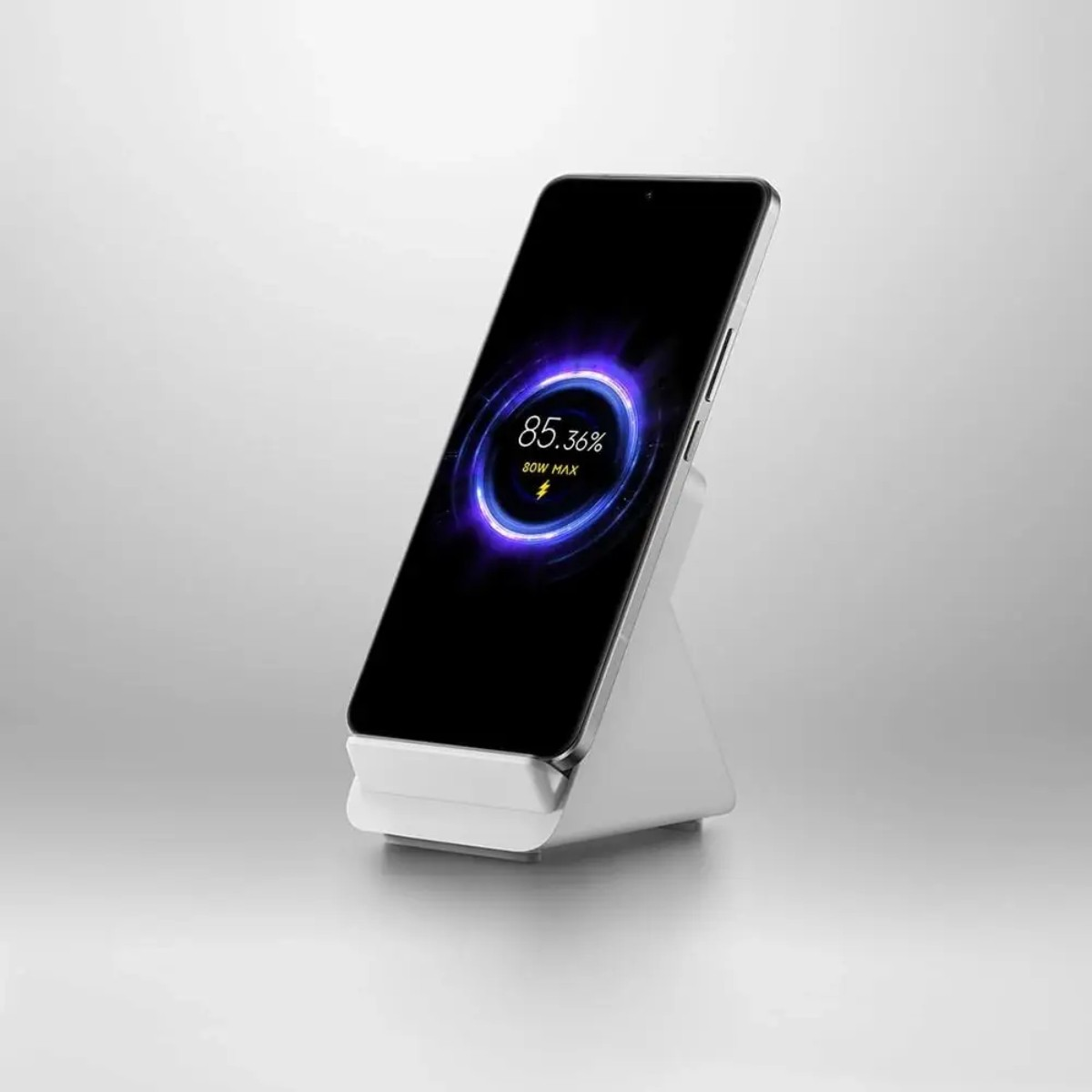 A phone charging on a white stand, showing 85.36% charge. The charger and phone are against a light backdrop.