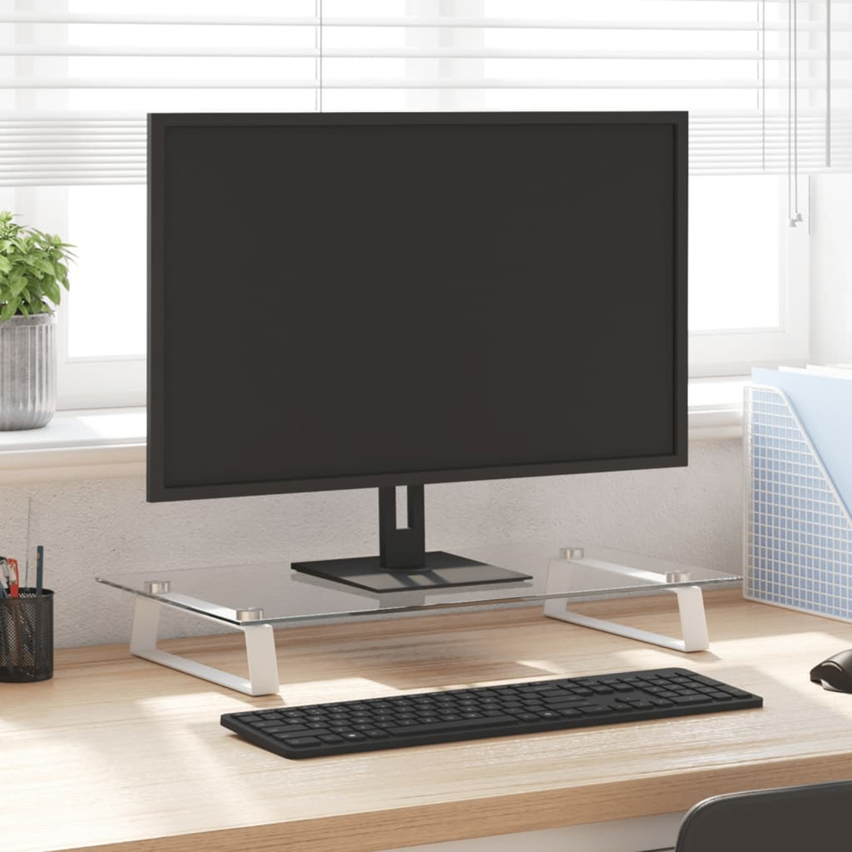 Ein Computermonitor auf einem Ständer aus klarem Glas mit weißen Beinen. Eine Tastatur und andere Dinge liegen auf dem Schreibtisch.