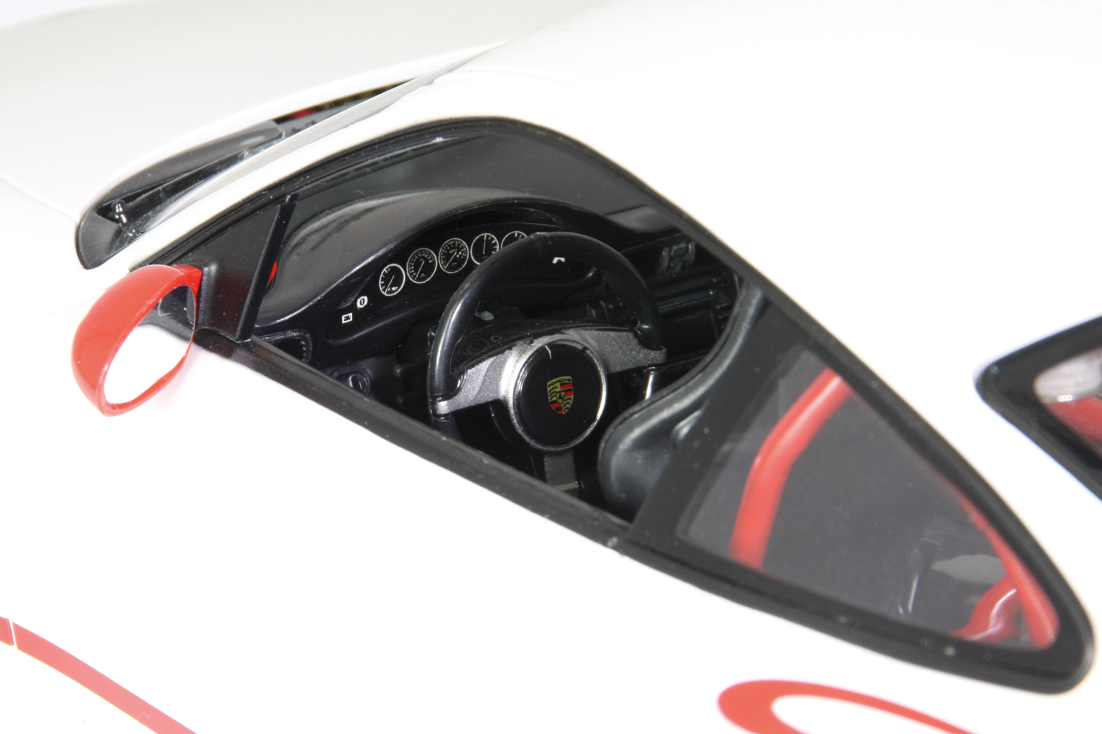 Zbliżenie wnętrza białego Porsche z czarną kierownicą i czerwonym lusterkiem bocznym.