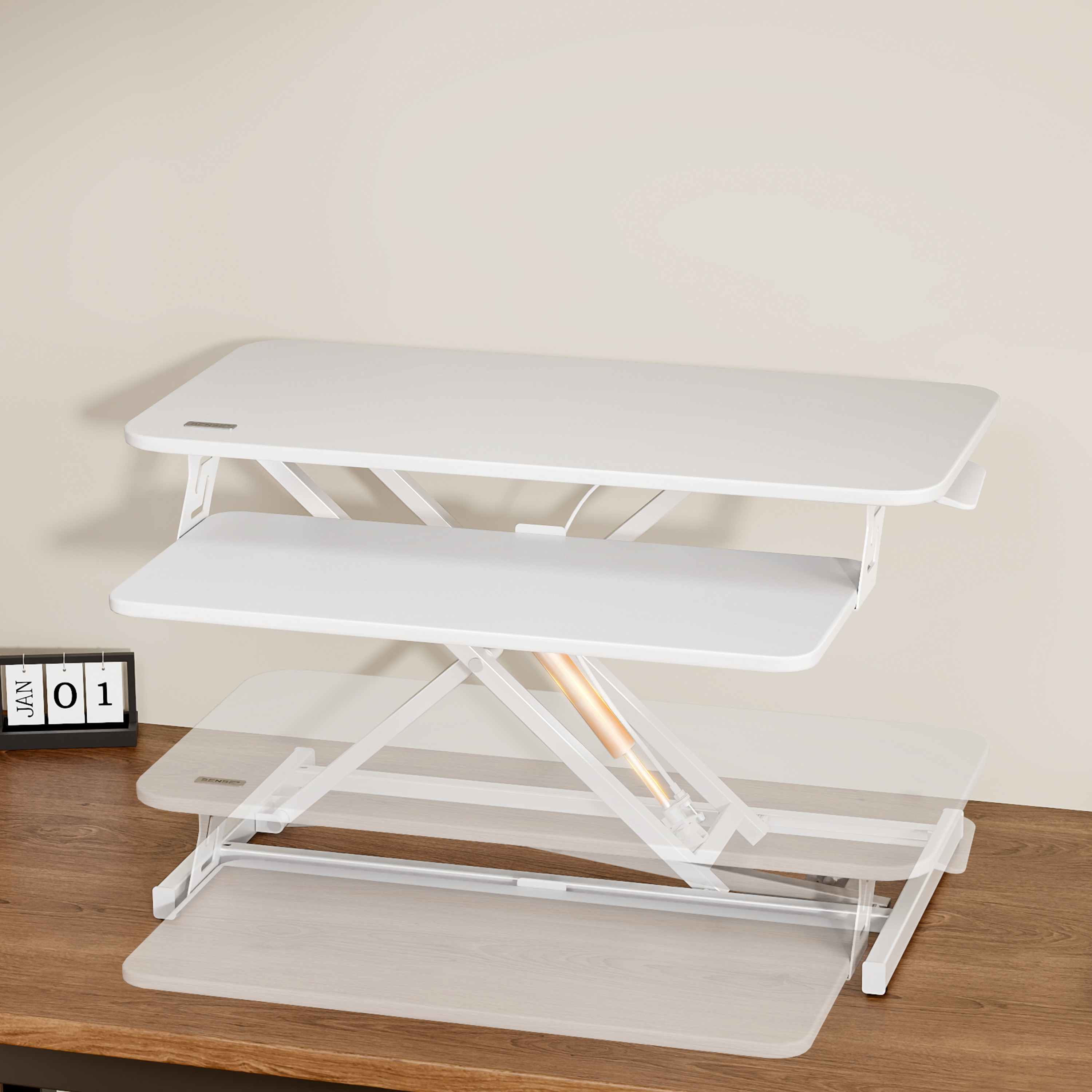 Escritorio blanco ajustable con tres niveles. Un calendario lee 01 de enero a la izquierda. Pared beige y superficie de madera.