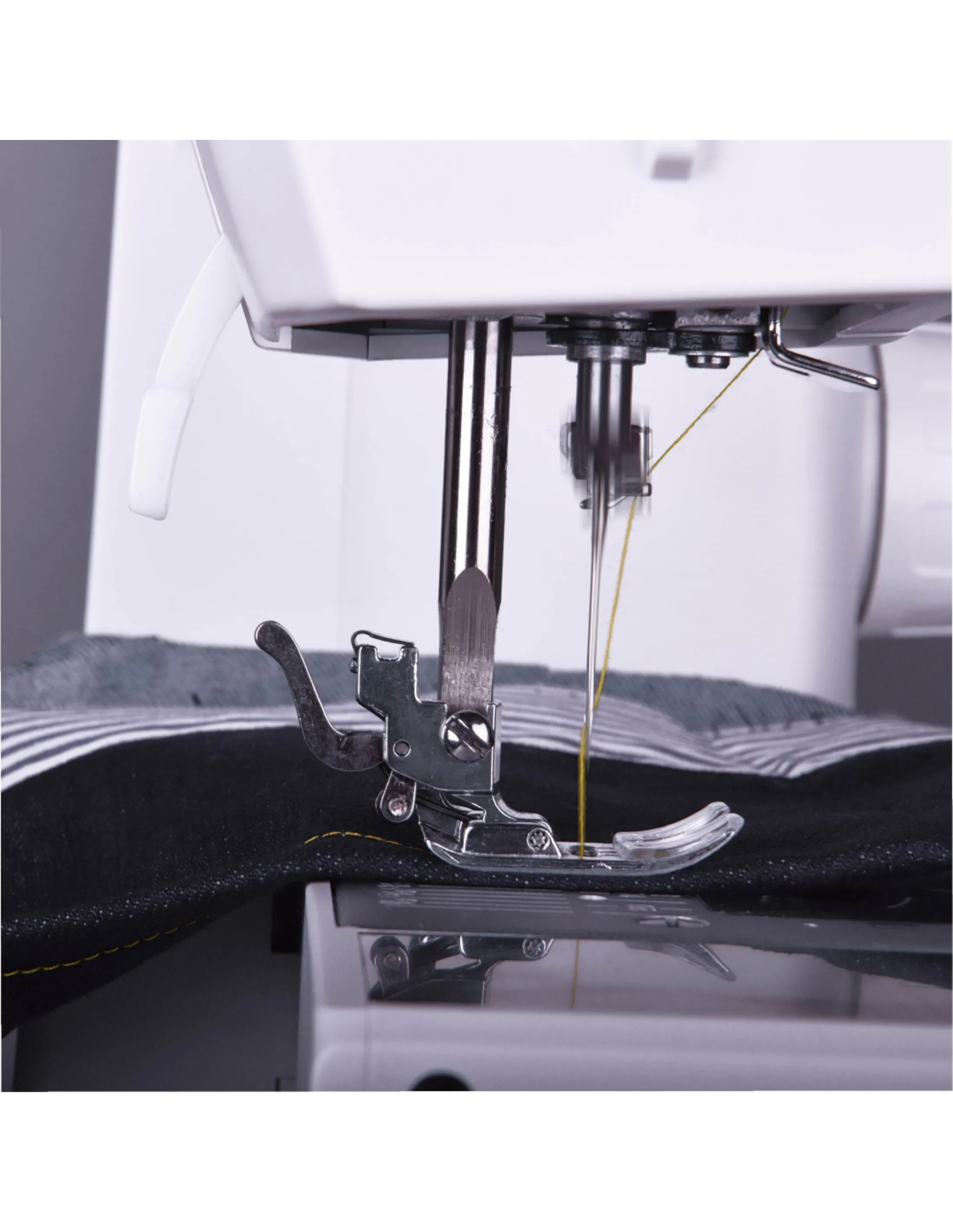 A sewing machine needle is in motion, stitching fabric. The machine is white, with metal parts and yellow thread.