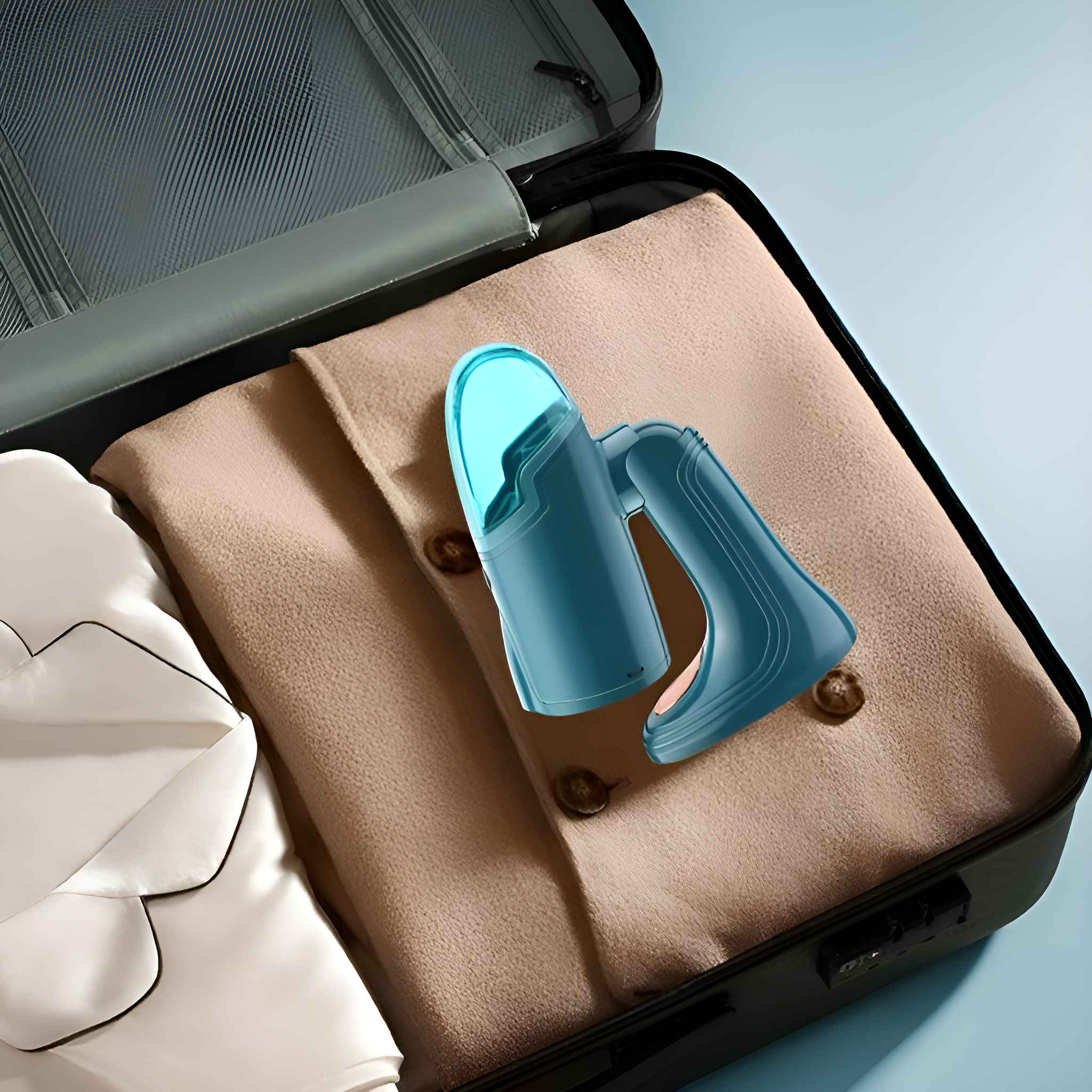 Ein tealfarbener Handdampfglätter in einem Koffer, mit beiger Kleidung. Er ist für die Reise gepackt.