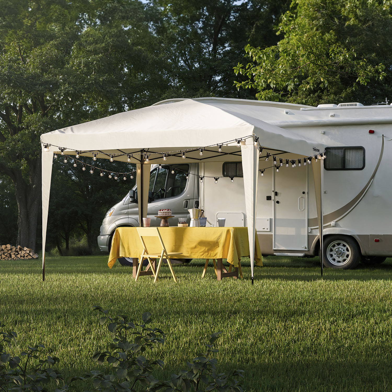 Camper geparkeerd naast een tent met een tafel op een grasveld.