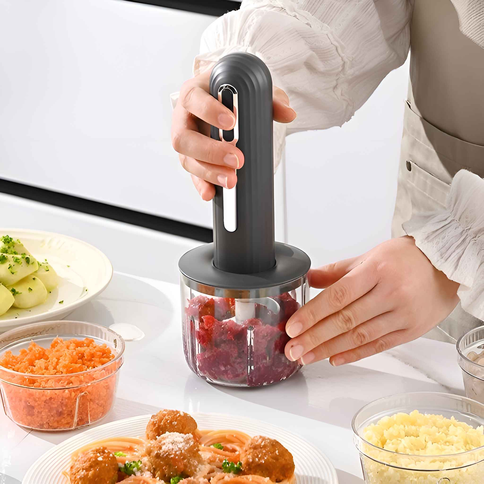 Eine Person benutzt einen weißen Zerkleinerer mit Essen, Tellern und Zutaten auf einem Tisch.