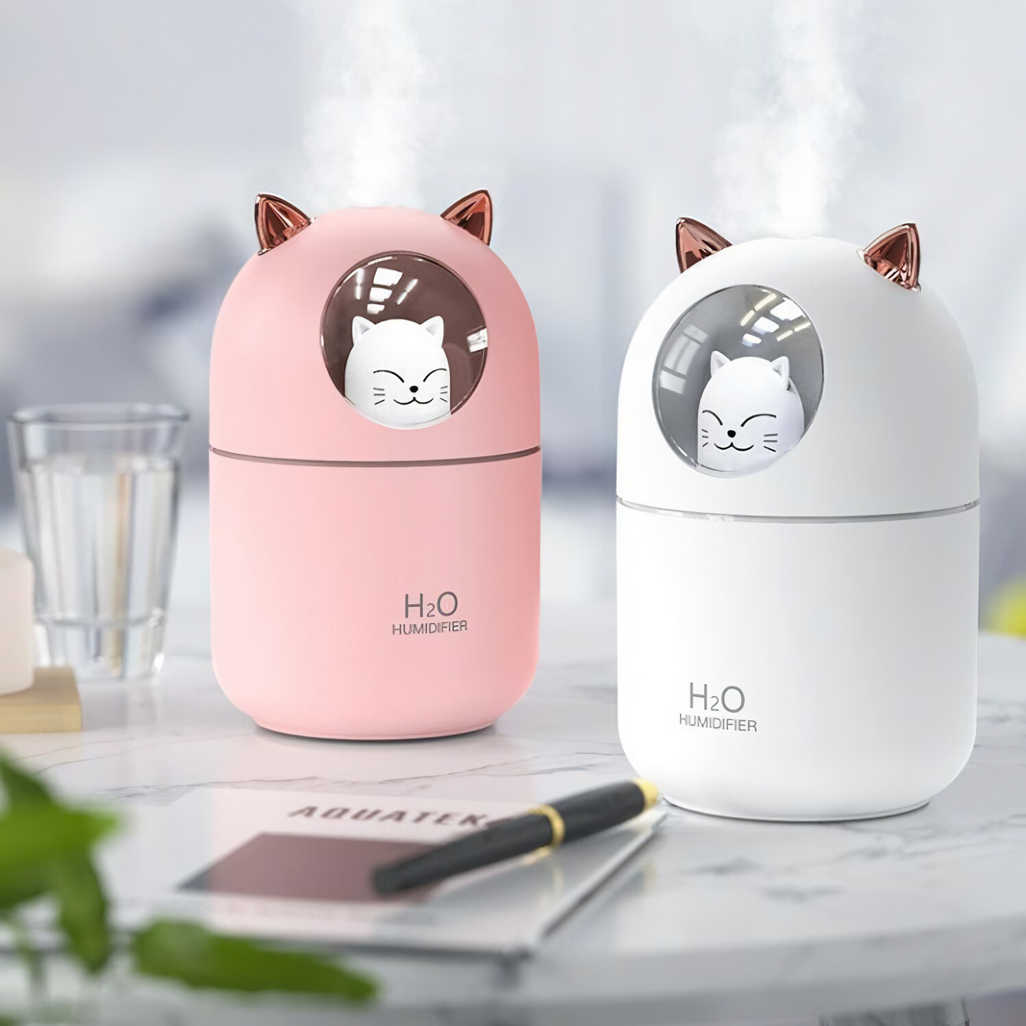 Zwei katzenförmige Luftbefeuchter, einer rosa und einer weiß, mit einer kleinen Katzenfigur in jedem.