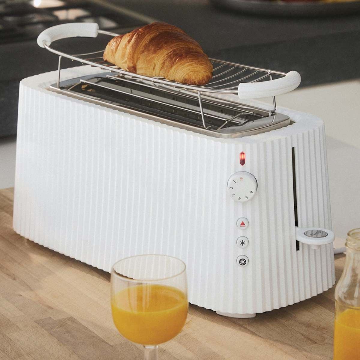 Tostapane bianco con croissant. Succo d'arancia. Tagliere in legno. Luce rossa accesa. Bicchiere di succo d'arancia. Bottiglia di succo.