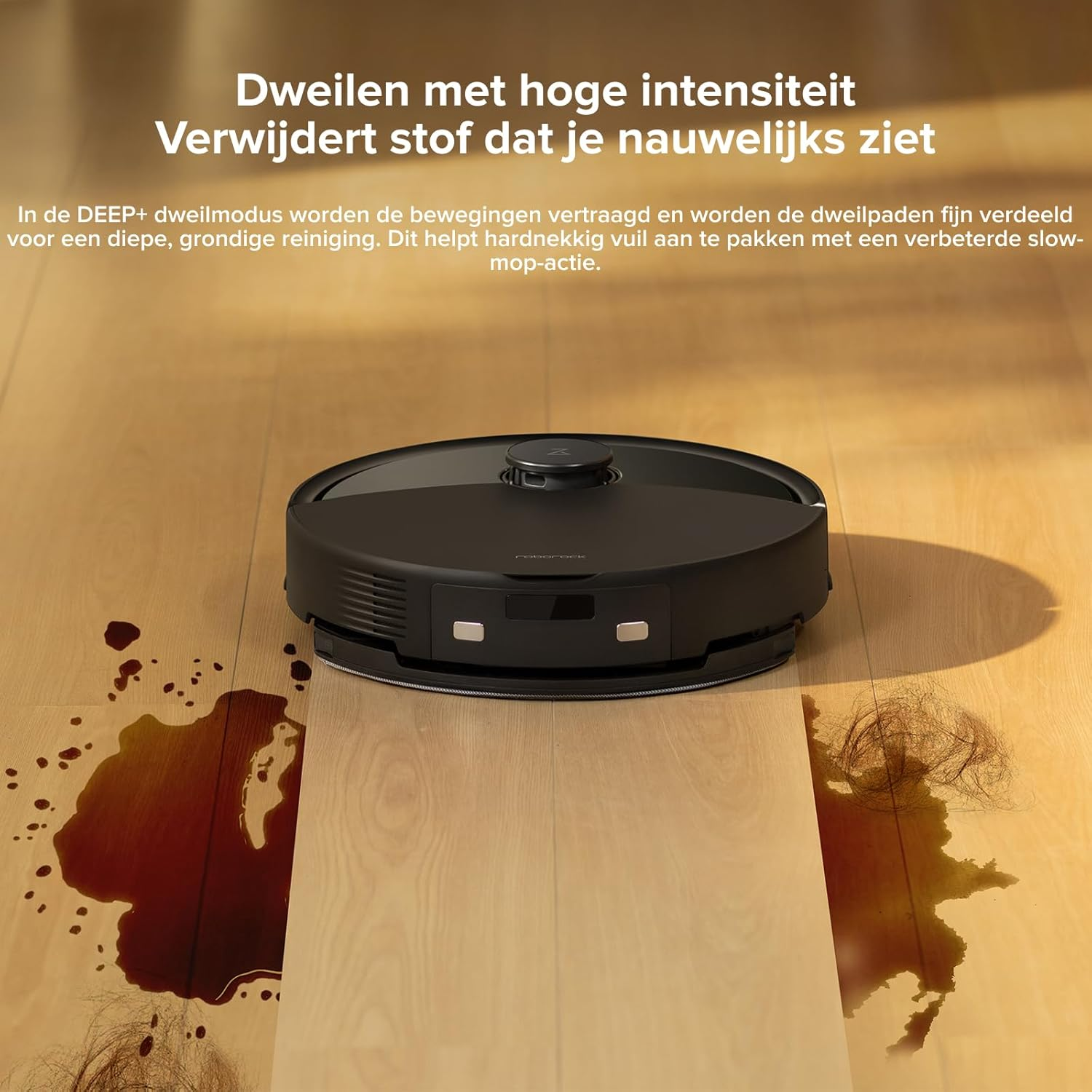 Un robot aspirateur noir sur un plancher en bois avec une tache d'eau et des cheveux.