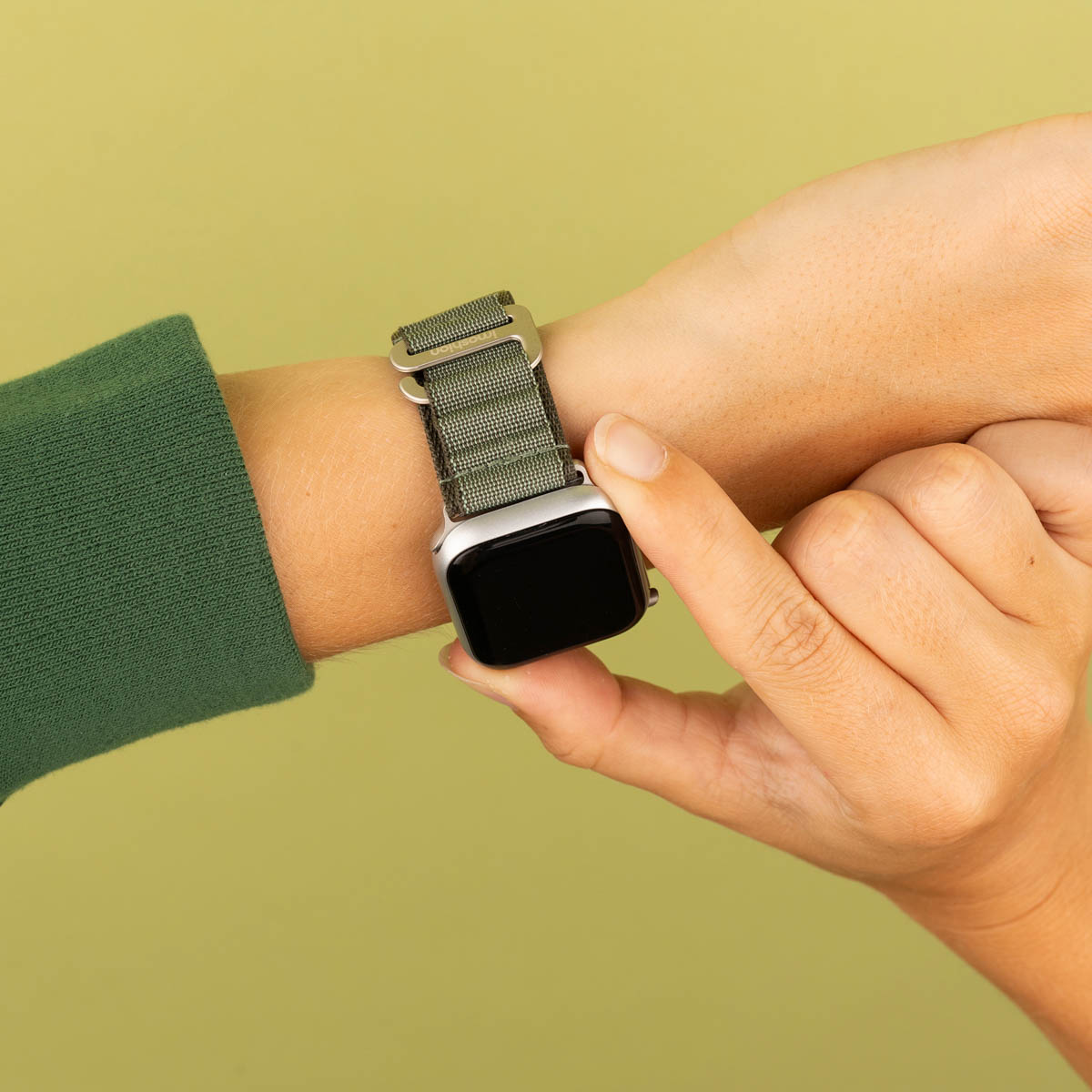 Een hand met een groene horlogeband op een lichtgroene achtergrond.