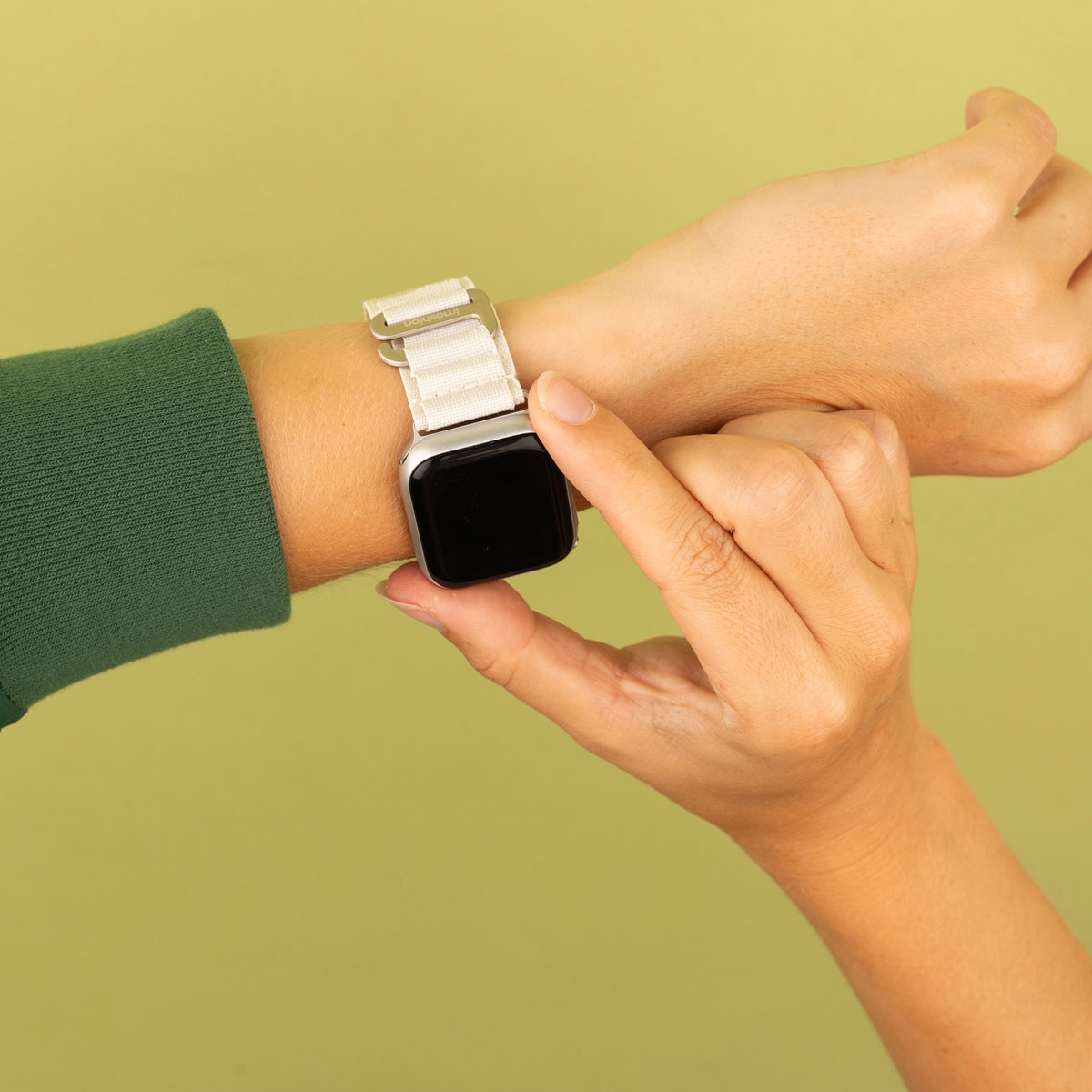 Een hand die een smartwatch met een witte band draagt, op een groene achtergrond.