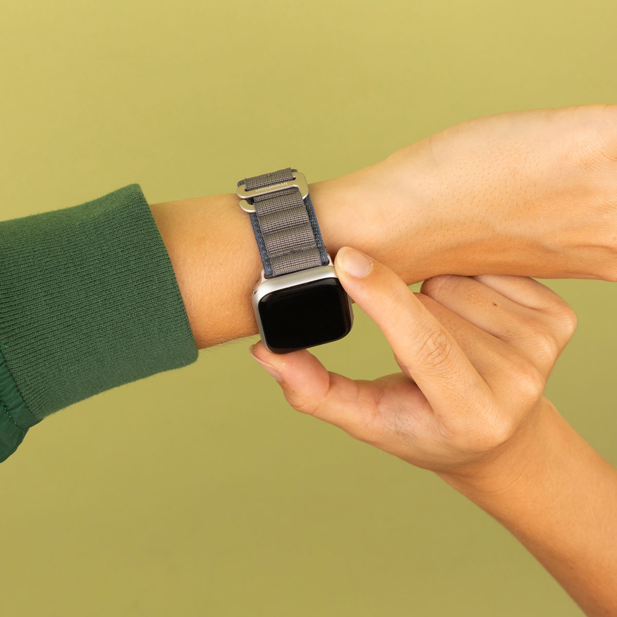 Een hand met een smartwatch met een grijze band, op een groene achtergrond.