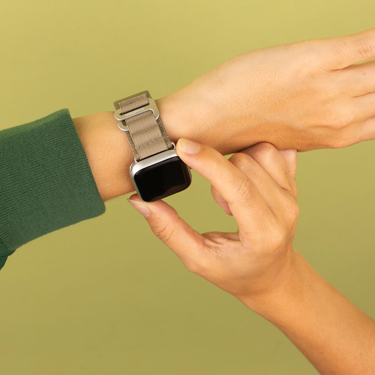 Een hand met een smartwatch met een grijze band, op een groene achtergrond.