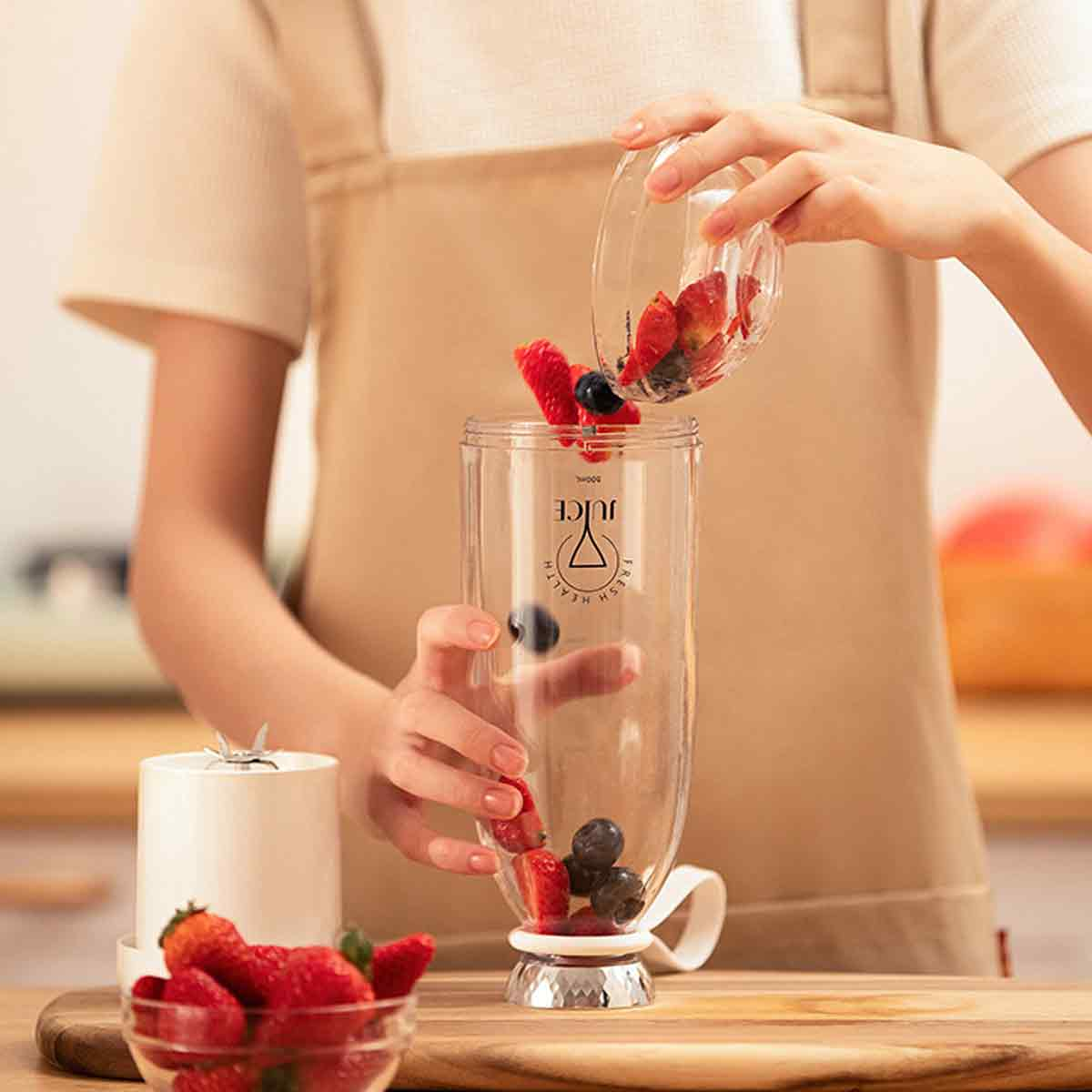 Eine Person gießt Früchte in einen tragbaren Mixer; Erdbeeren und Blaubeeren sind sichtbar.