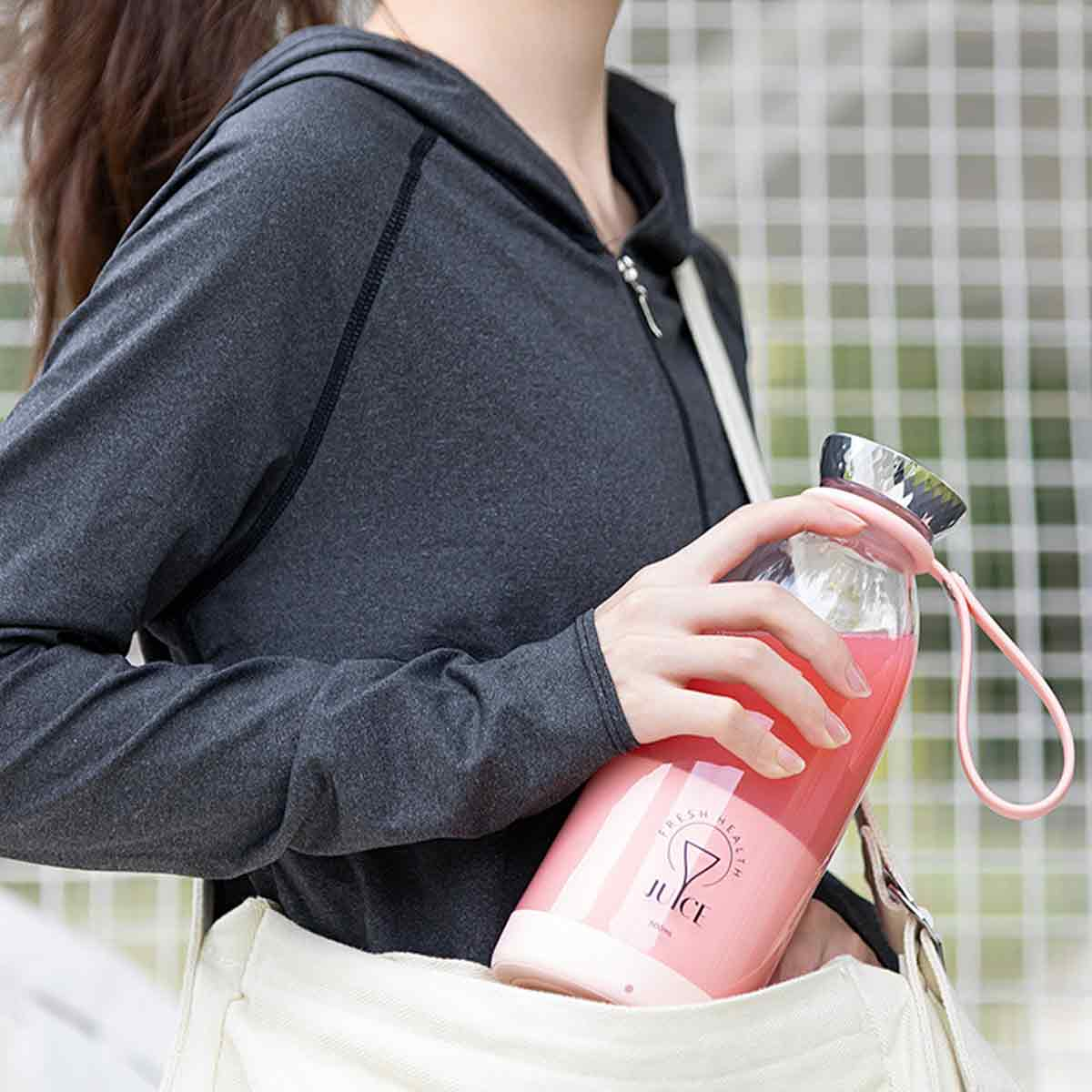 Frau hält eine rosa Saftflasche in der Hand, mit einer weißen Tasche an ihrer Seite.