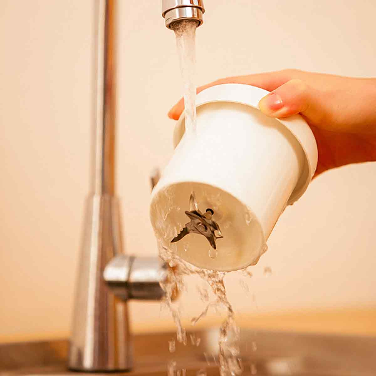 Wasser, das über die Klinge eines Mixers läuft, gehalten von einer Hand.