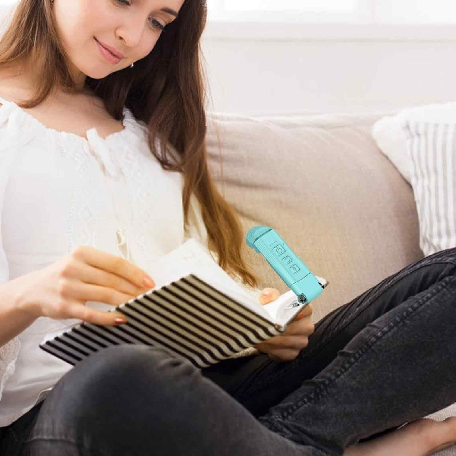 Eine Frau sitzt auf einem Sofa und liest ein Buch, wobei sie eine blaue Leselampe benutzt.