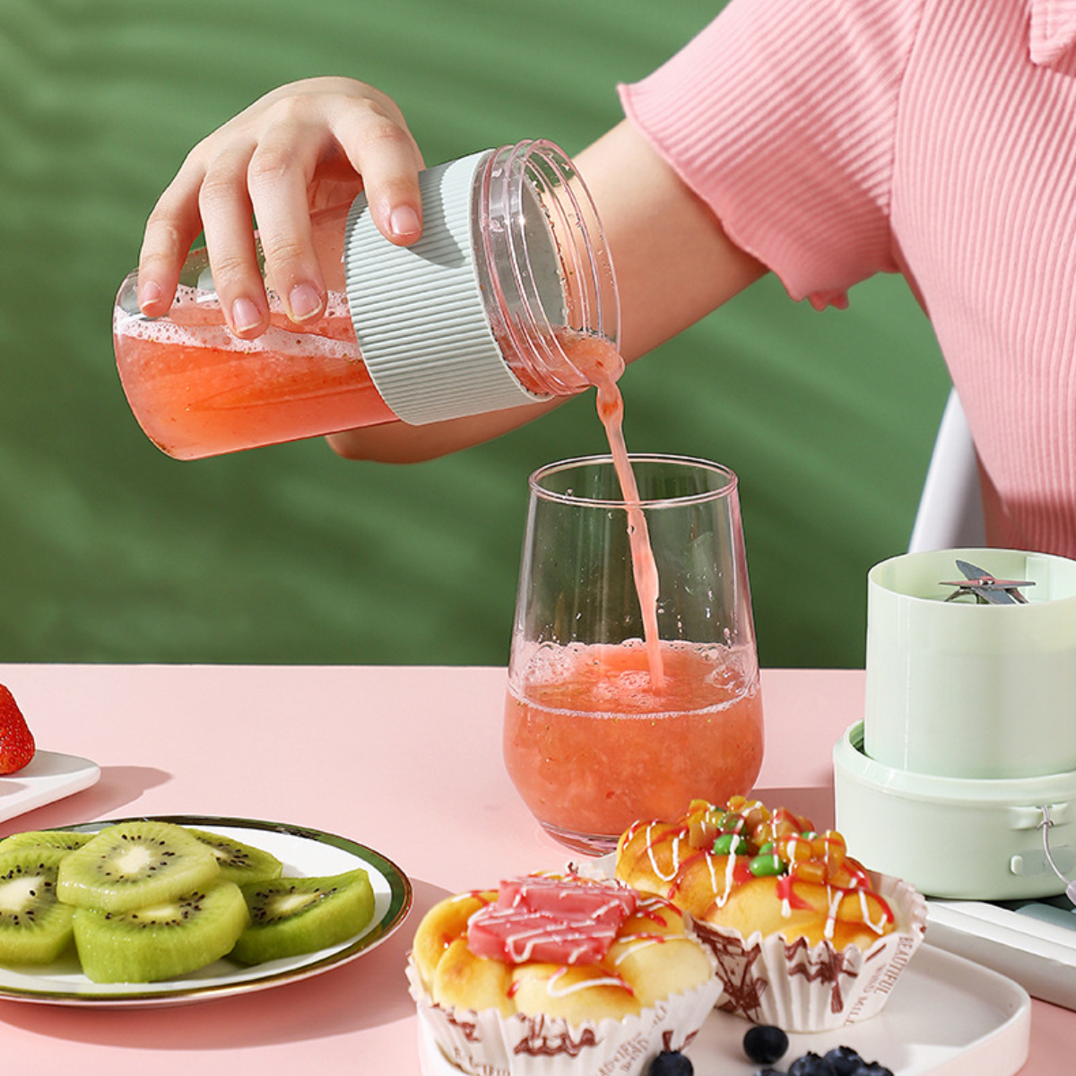 Eine Person gießt pinkfarbenen Smoothie aus einem Mixer in ein Glas. Kuchen und Kiwischeiben.