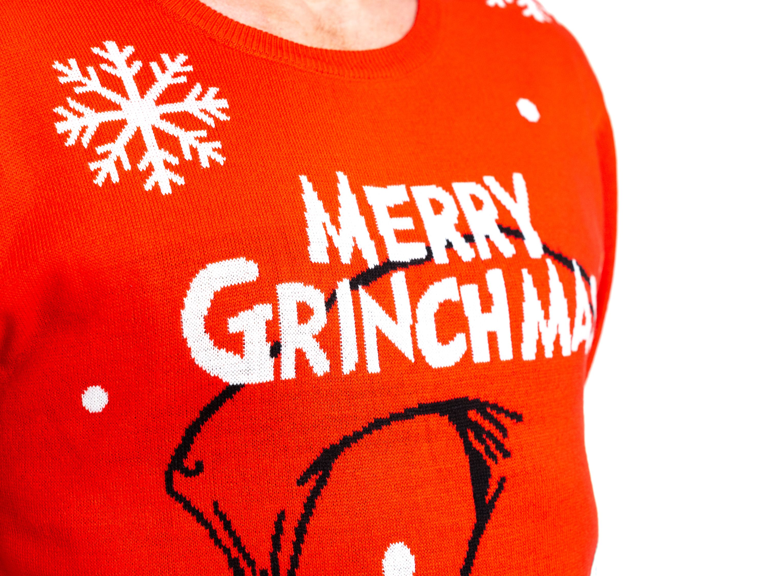 Roter Weihnachtspullover mit „MERRY GRINCHMAS“ und Grinch-Gesicht. Schneeflocken. Weißer Hintergrund.