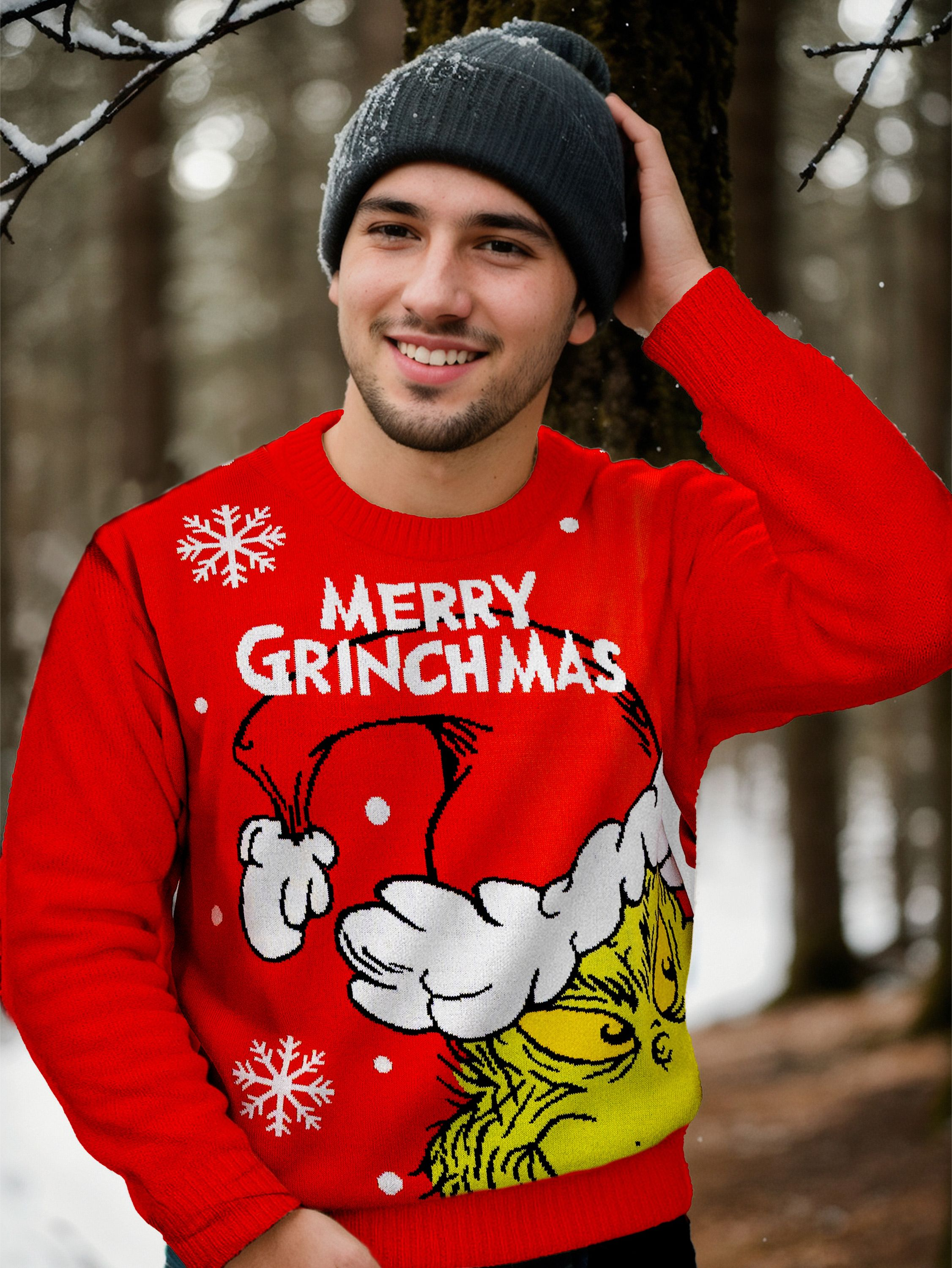 Ein Mann trägt einen roten Pullover mit Grinch-Design, graue Mütze. Er lächelt.