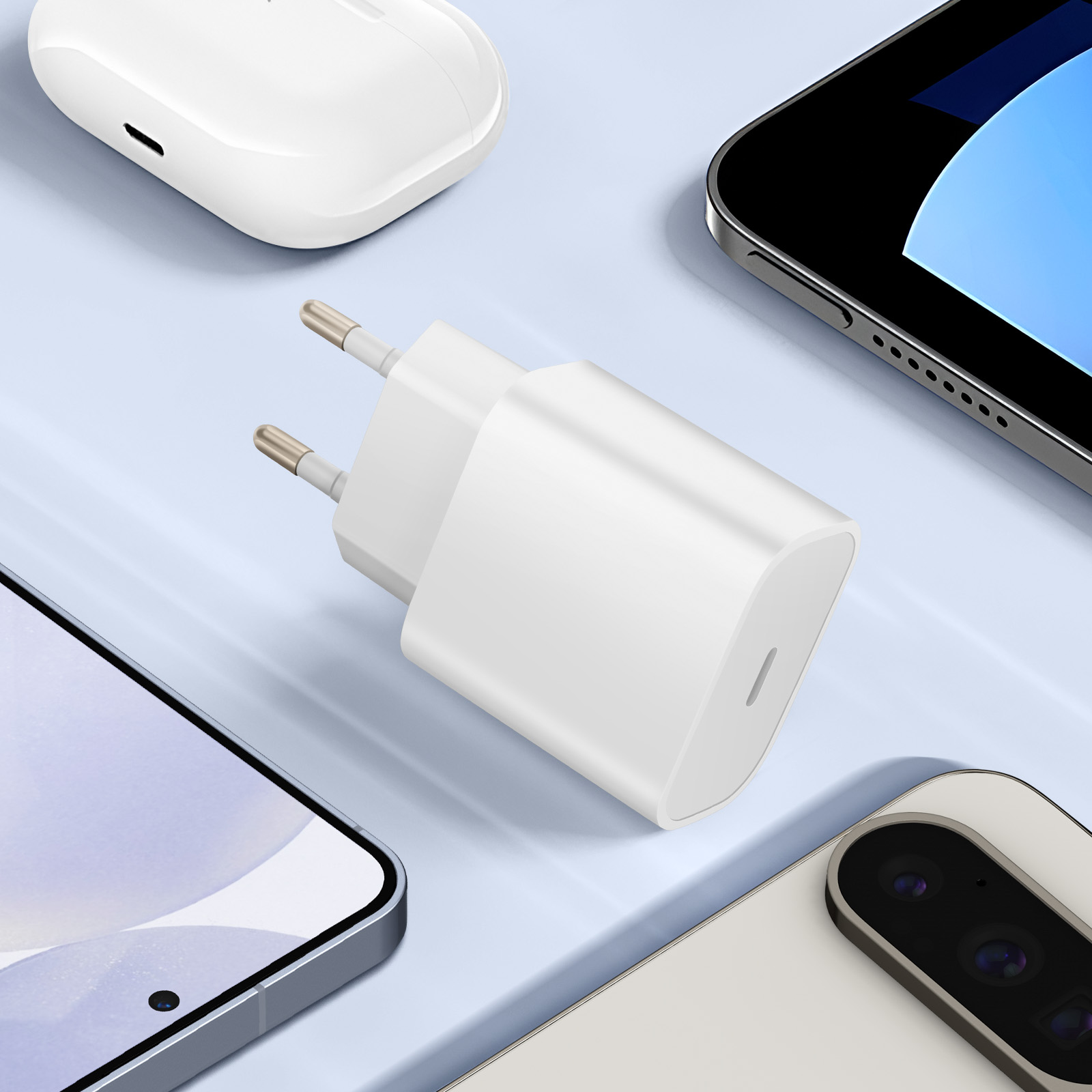 Un caricabatterie bianco con due spinotti argentati, vicino a un telefono, auricolari e un altro dispositivo su una superficie azzurra.