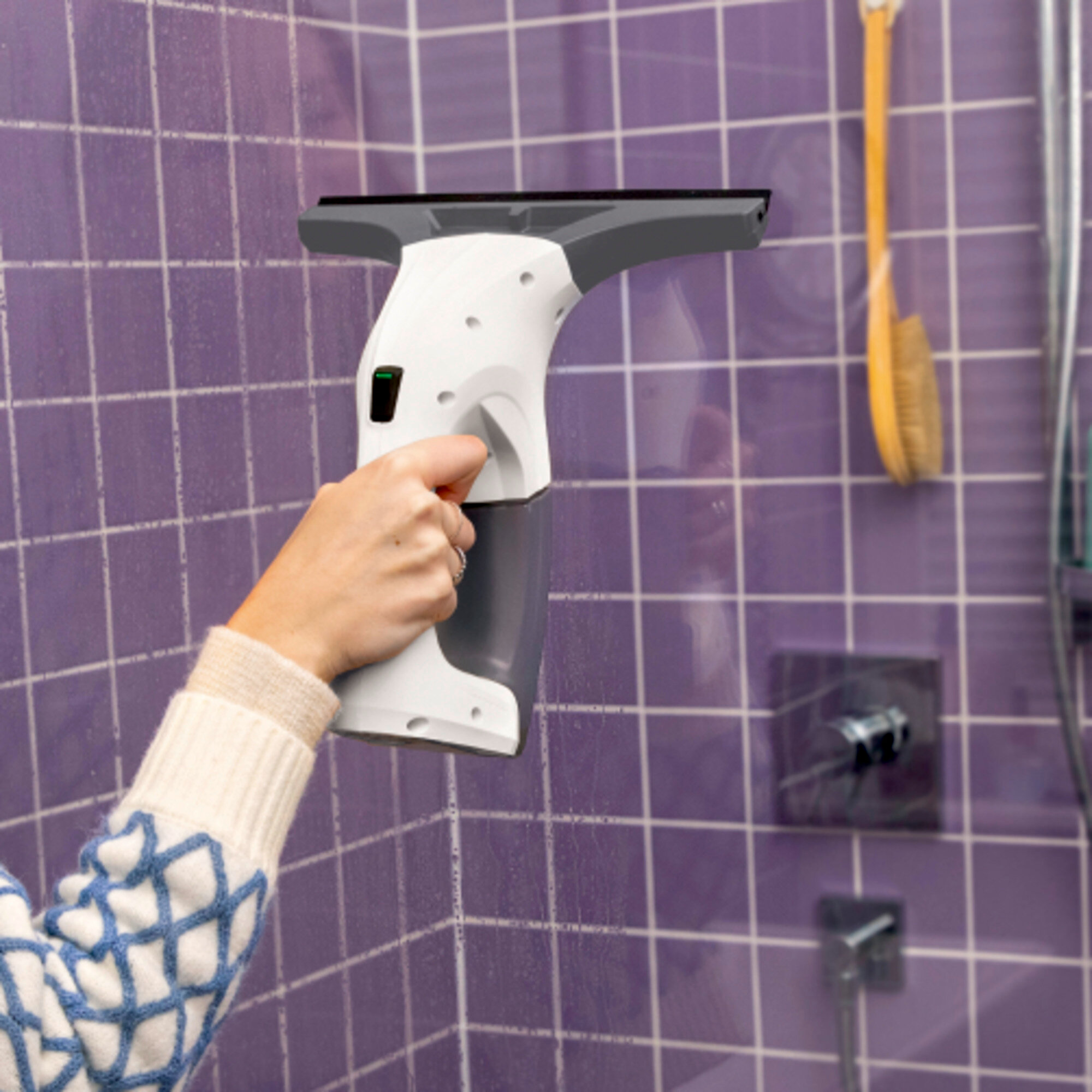 Een persoon maakt een paarse tegelmuur schoon met een witte en grijze ruitenreiniger. Een borstel hangt op de achtergrond.