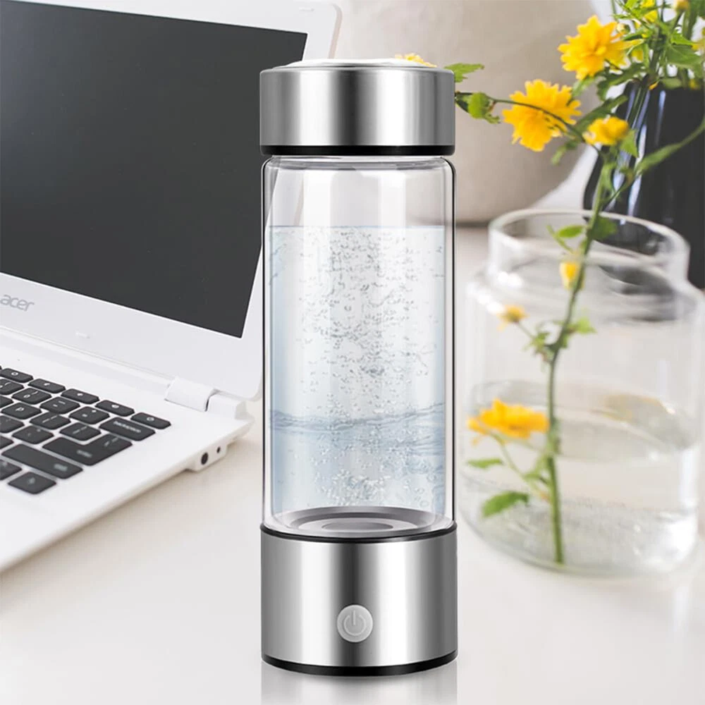Eine durchsichtige Wasserflasche mit silbernen Akzenten steht auf einem Schreibtisch in der Nähe eines Laptops und Blumen und verbindet Technologie mit Natur.