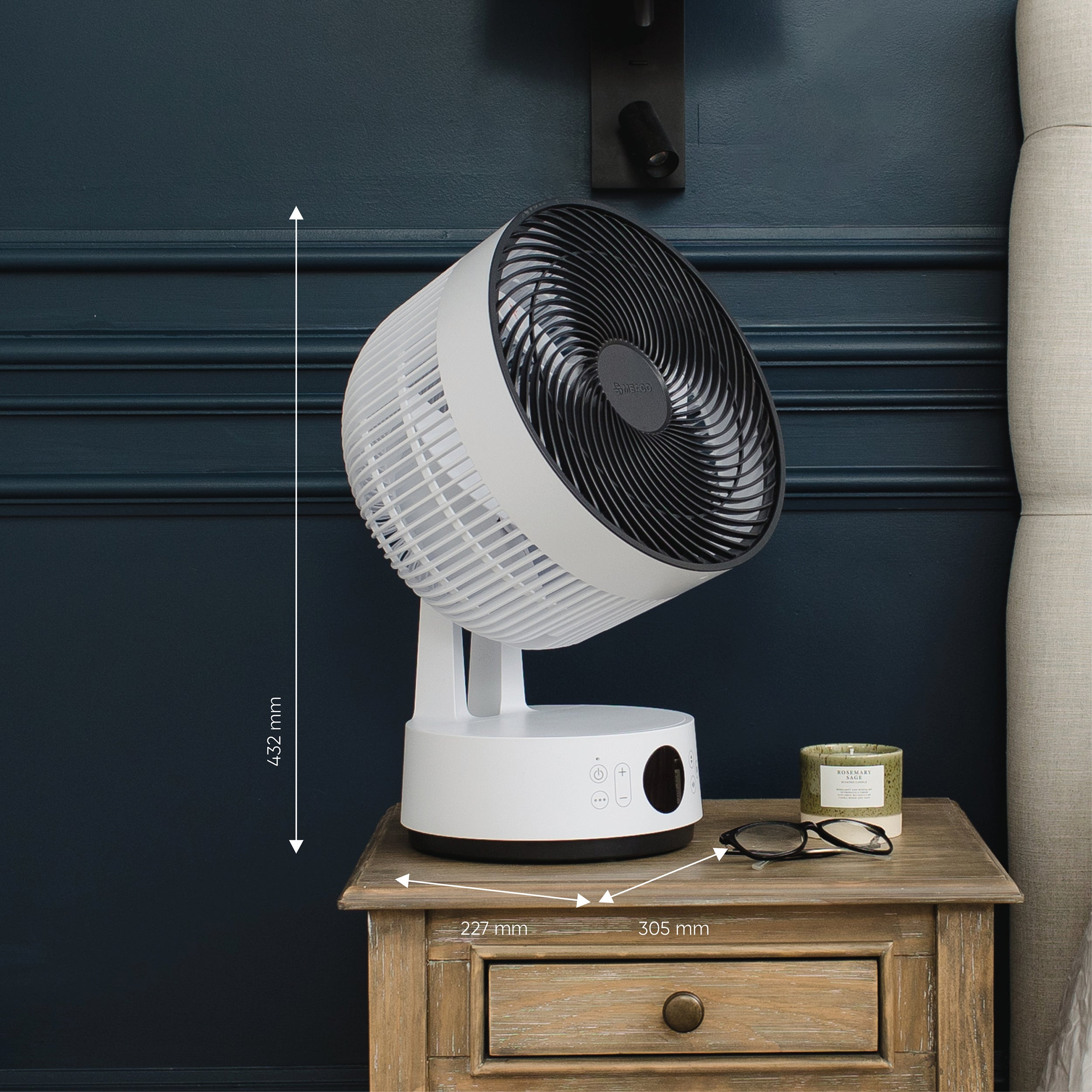 Biało-czarny wentylator stoi na drewnianej szafce nocnej. Wyświetlane są wymiary. Na szafce jest świeca i okulary.