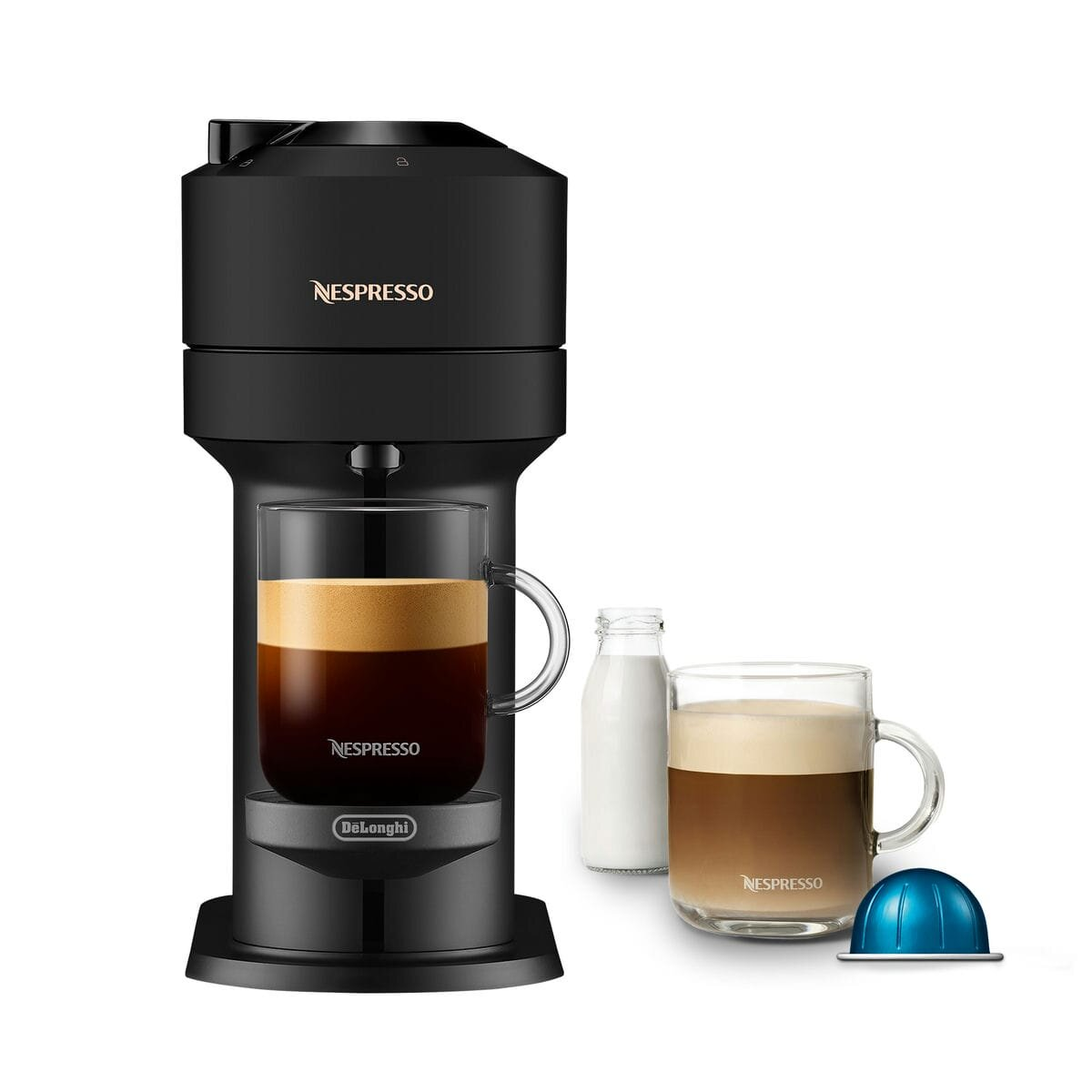 Máquina Nespresso negra con dos tazas de café. Botella de leche y cápsula al lado.