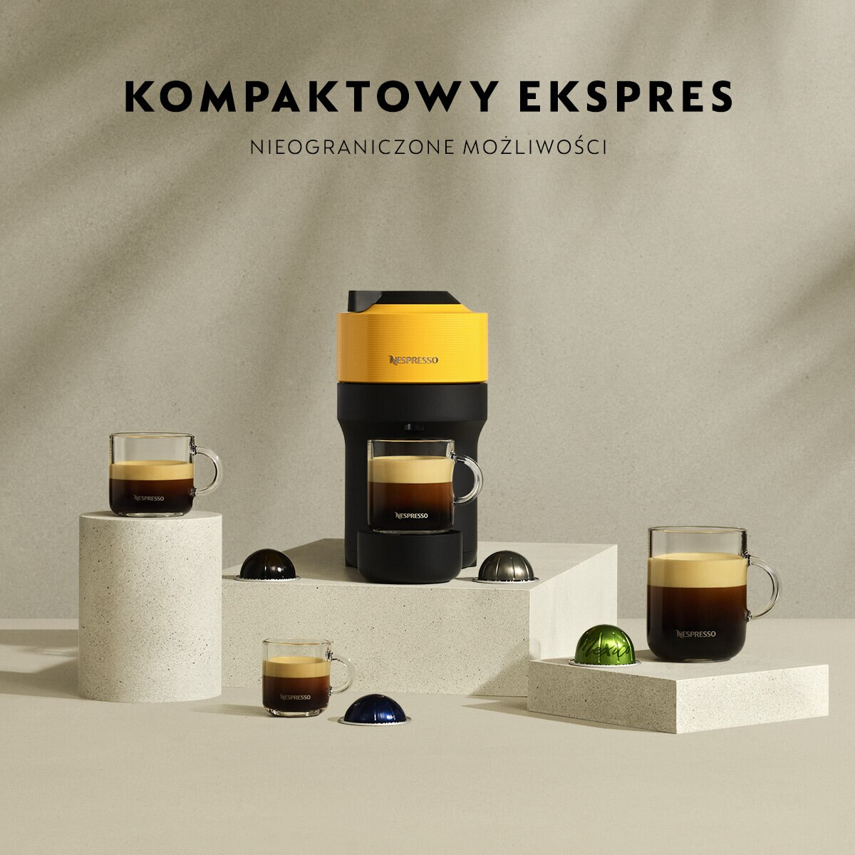 Eine gelb-schwarze Nespresso-Kaffeemaschine mit Kaffeetassen. Der Text oben lautet 'KOMPAKTOWY EKSPRES'.