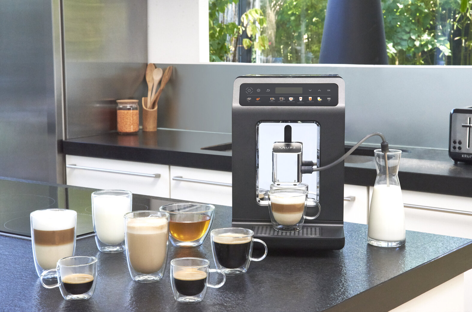 Ekspres do kawy z różnymi napojami kawowymi w filiżankach. Dzbanek z mlekiem obok ekspresu. Tło kuchni.