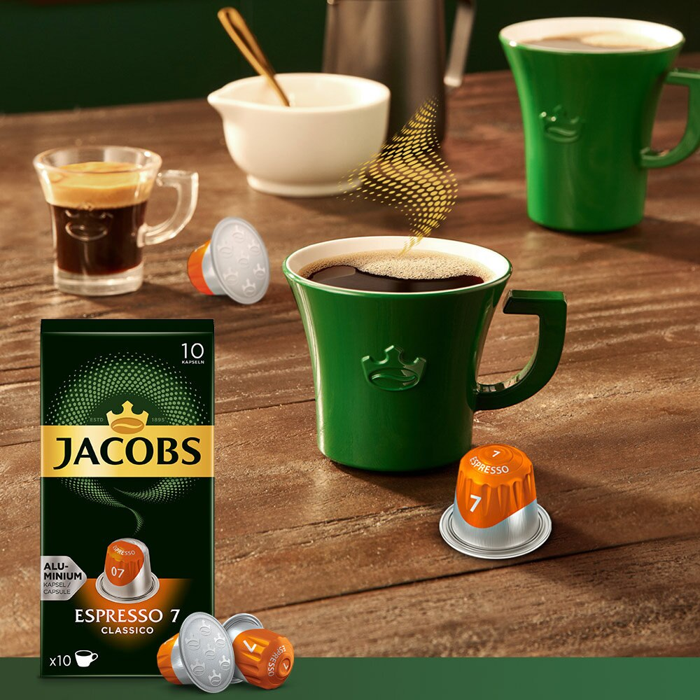 Capsule di caffè, Jacobs Espresso 7 e tazze di caffè con caffè, su un tavolo, con una scatola verde Jacobs.