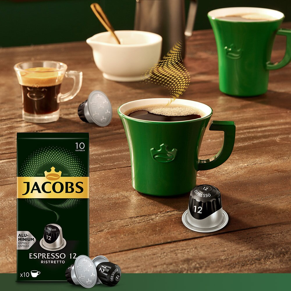 Kaffeekapseln, Kaffeetassen und eine Schachtel Jacobs Espresso 12 Ristretto auf einem Holztisch.