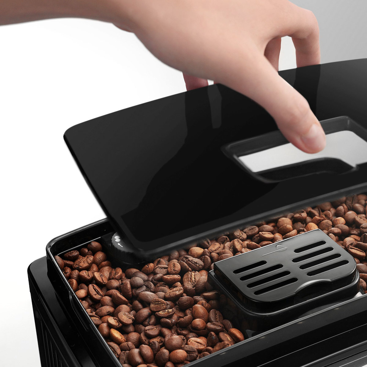 Een hand die het bonenreservoir opent op een DeLonghi koffiemachine, met koffiebonen.