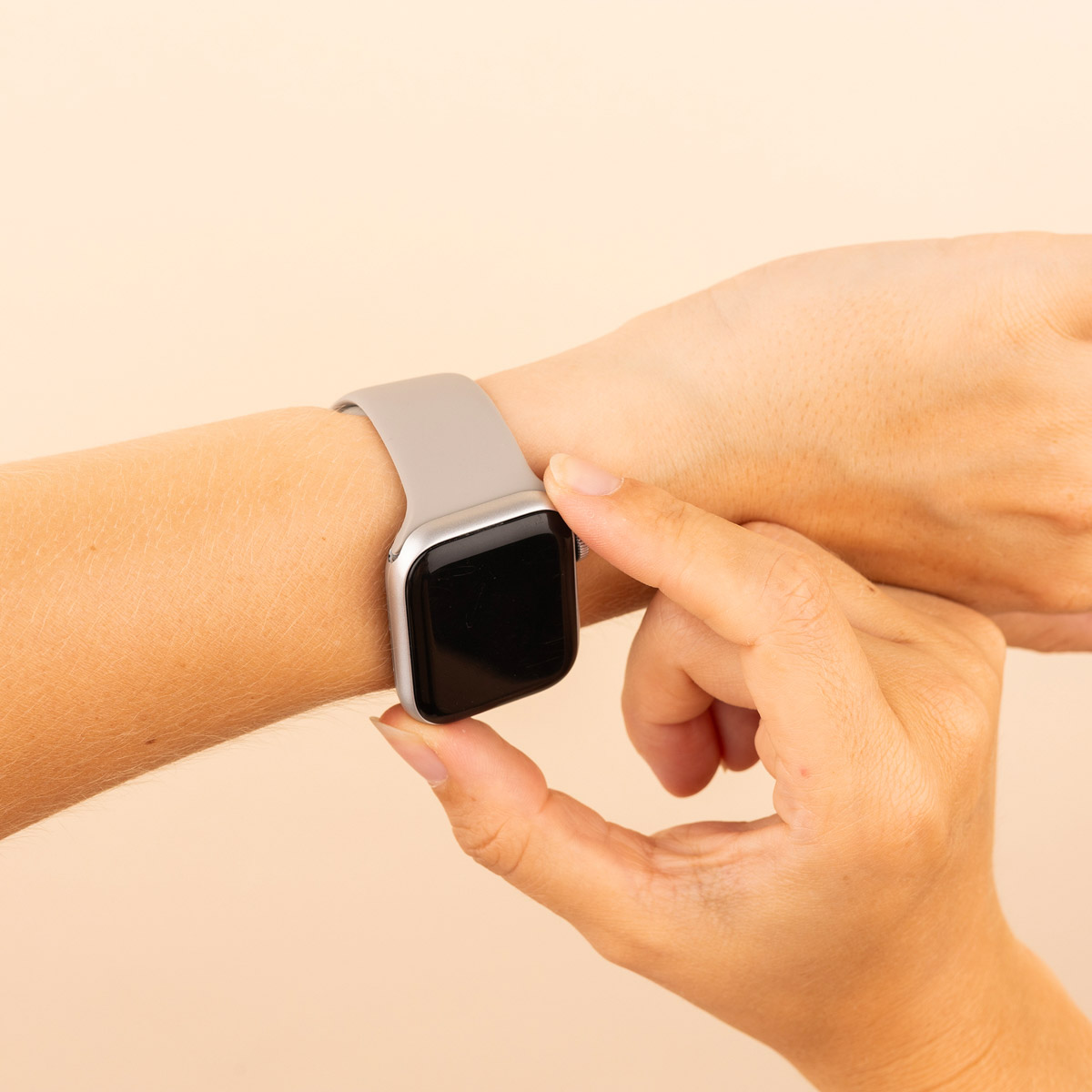 A person's wrist with a silver Apple Watch. The watch has a black screen and a gray band.