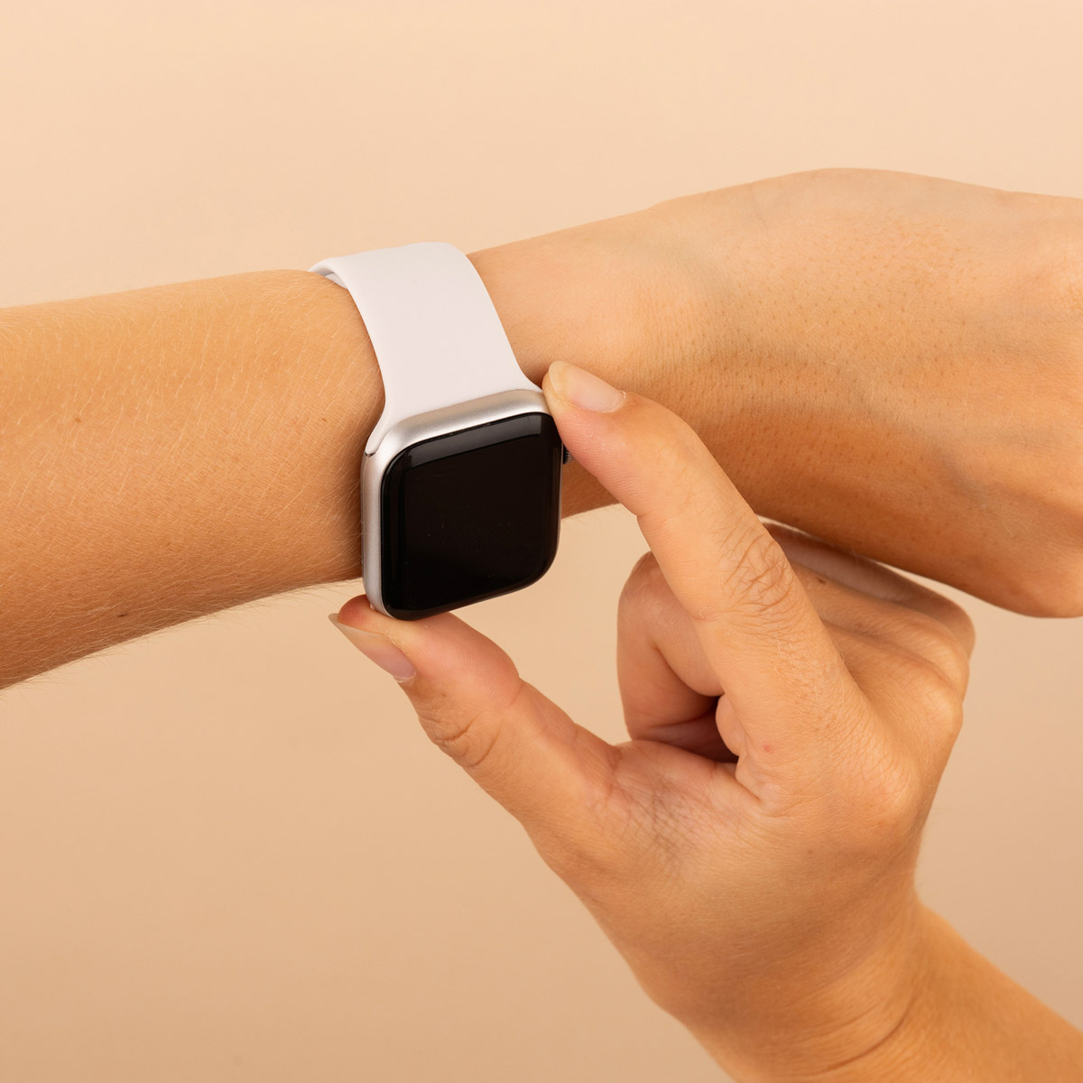 A wrist with a silver Apple Watch. The watch has a black screen and a white band.
